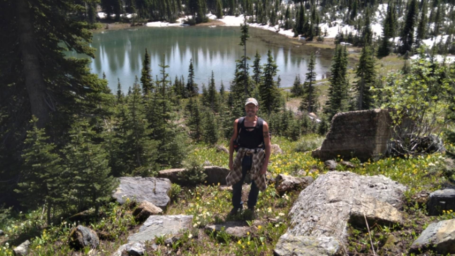hiker stading on a rock strewn hillside with mountain lake in the background.