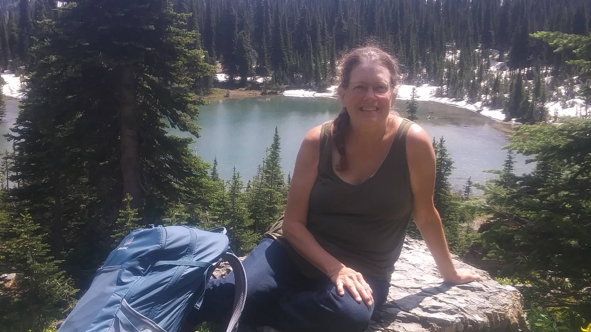 A woman sittin on a rock with a mountain lake in the background.