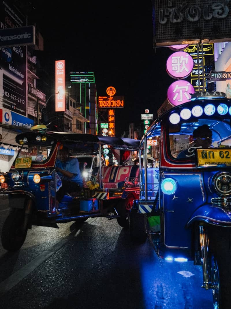 Two blue tuk-tuks at night with neon signs