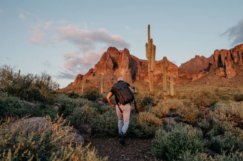 A hiker climbs a desert trail towards mountains.