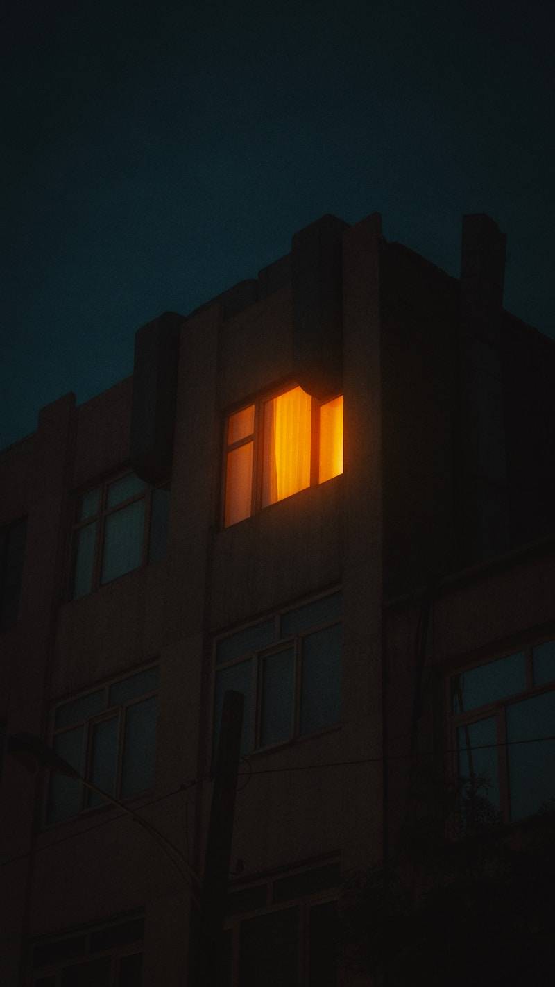 A building at night with one lit window.
