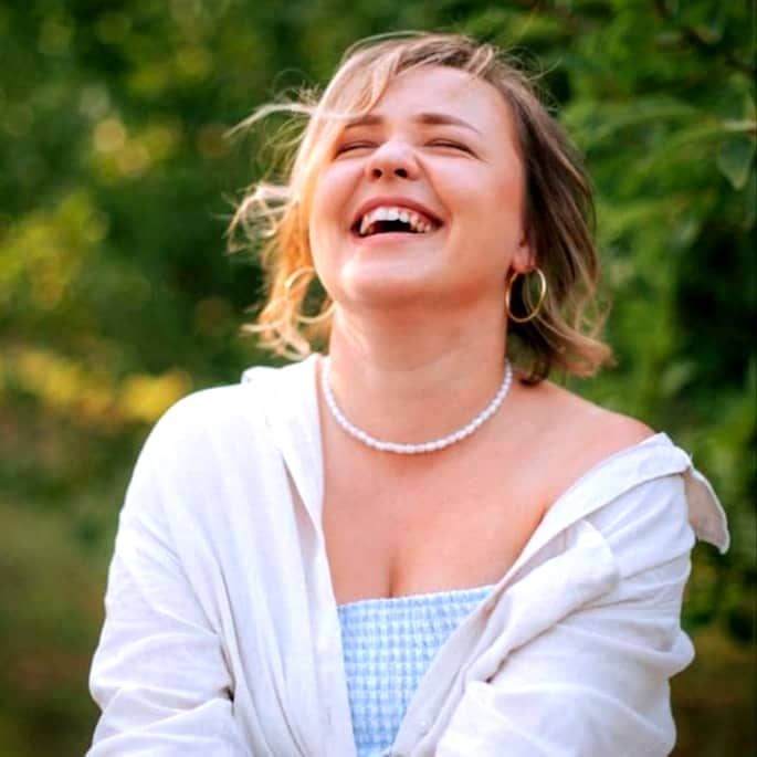 A woman laughing outdoors in a park.