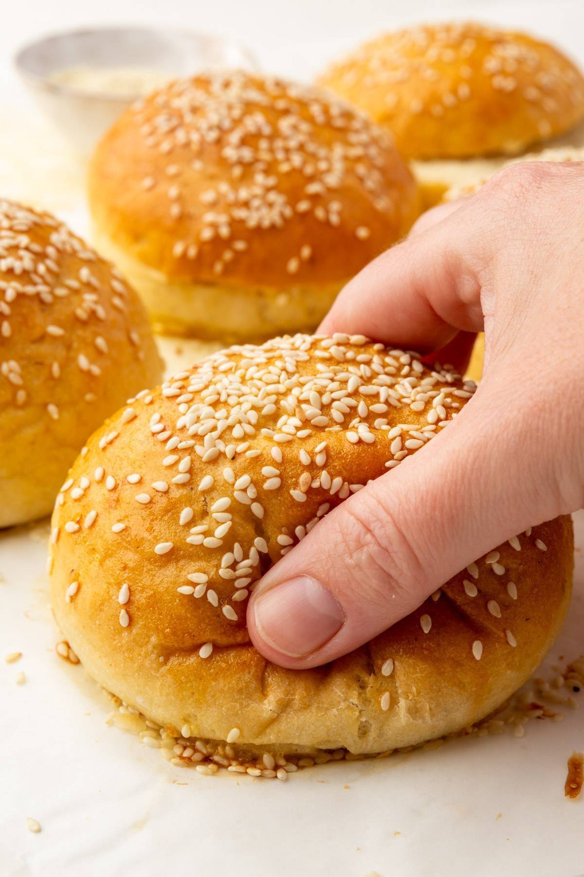 A gluten-free hamburger bun with sesame seeds being squished by someone's hand. 