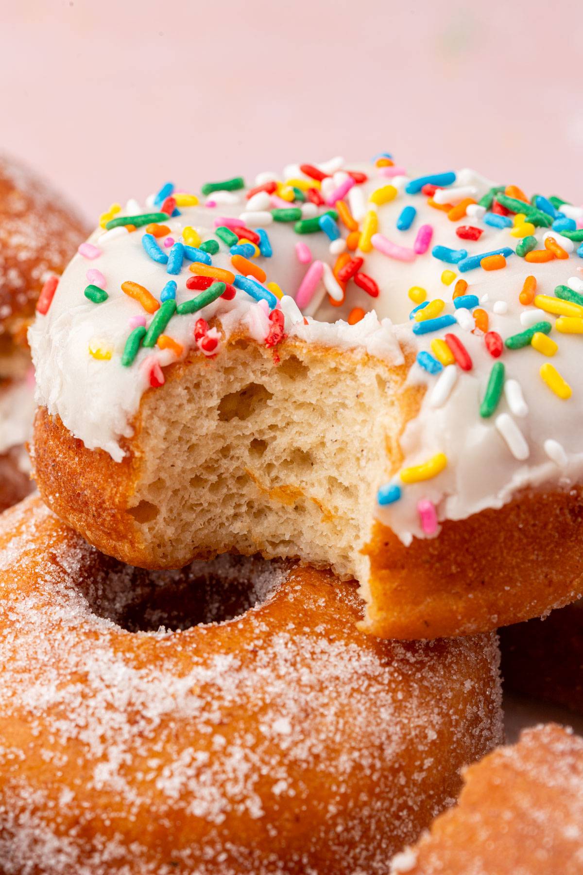 A gluten-free donut with vanilla frosting and rainbow sprinkles with a bite taken out of it. 