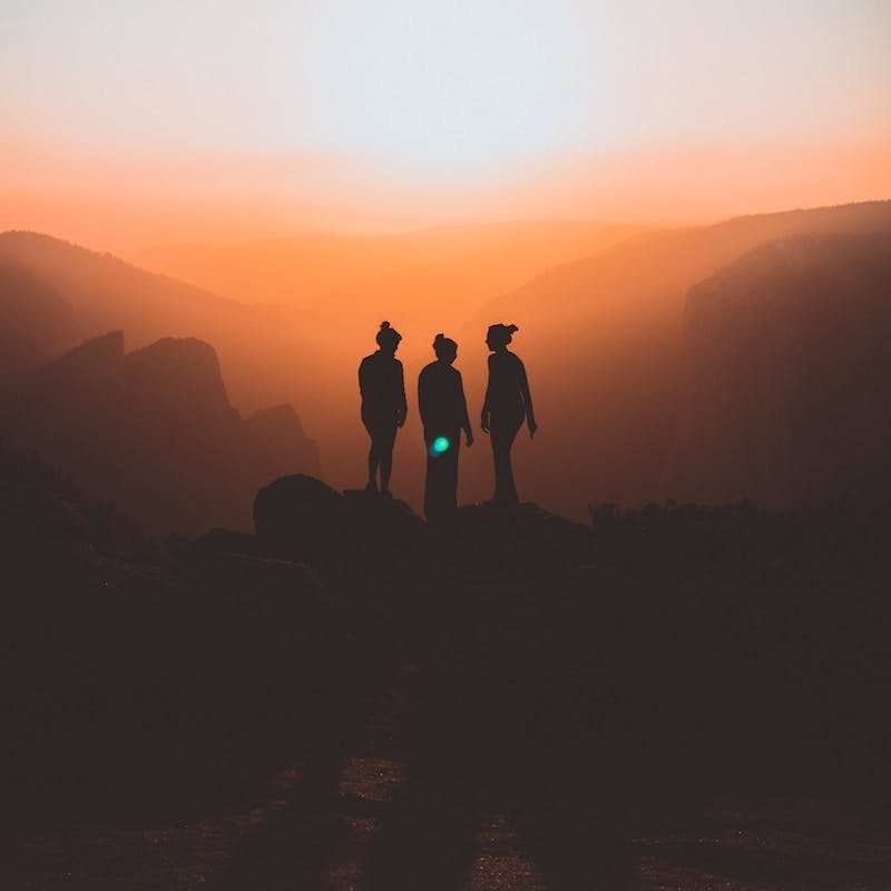 silhouette of three people up on mountain cliff