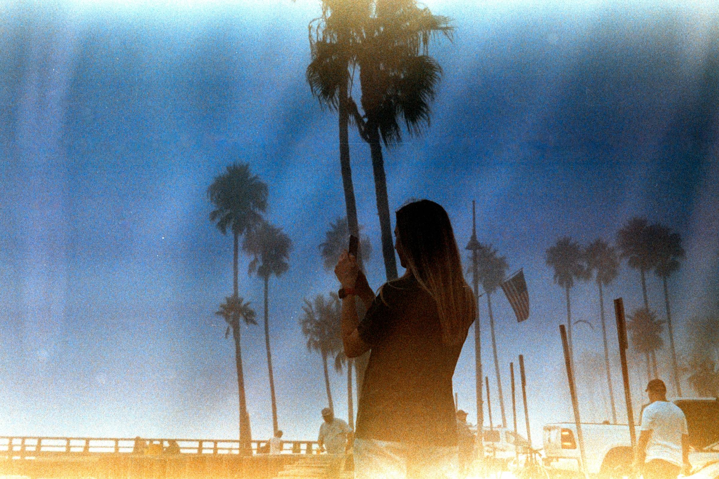 A faded image of a woman faced away from the camera in front of palm trees