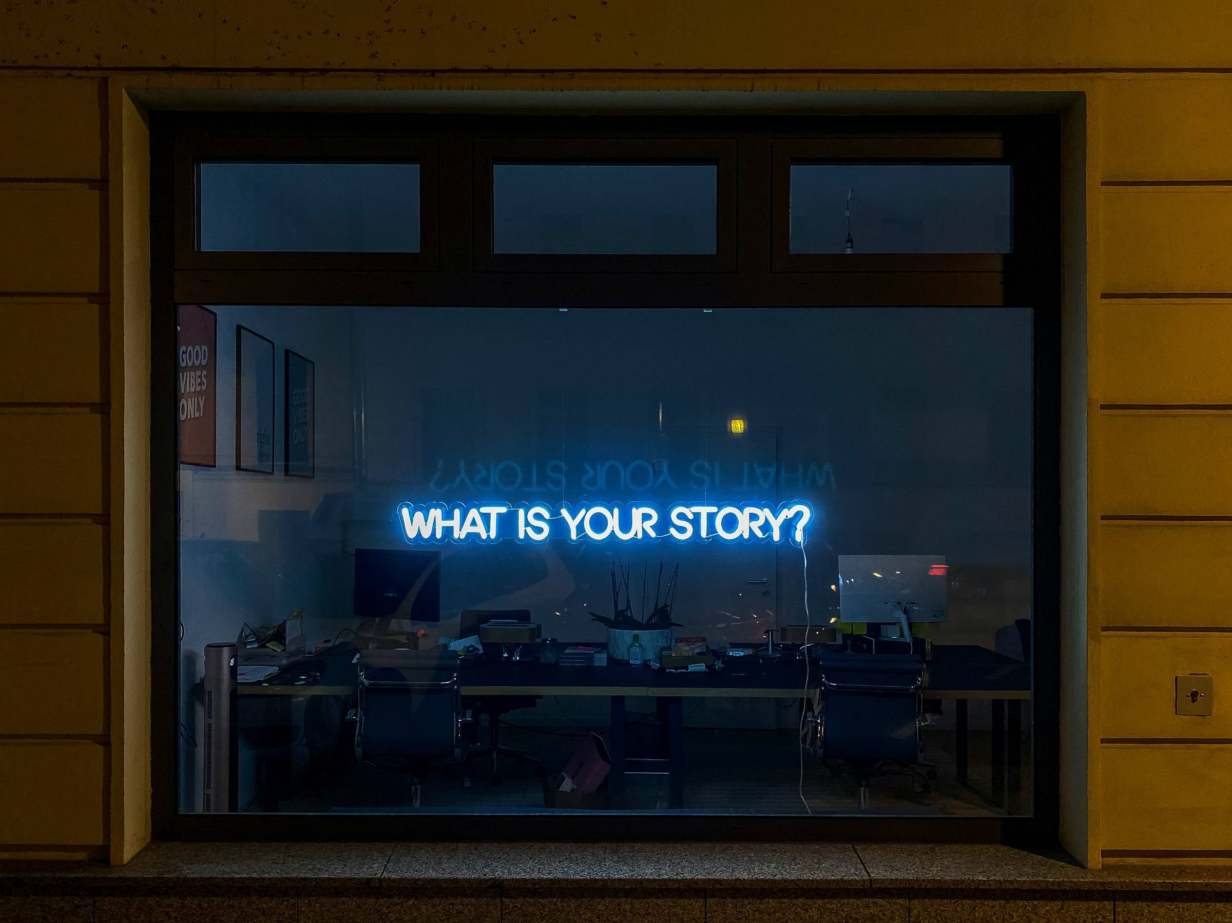 The image is of a dark window with neon letters that reads "What is your story?"