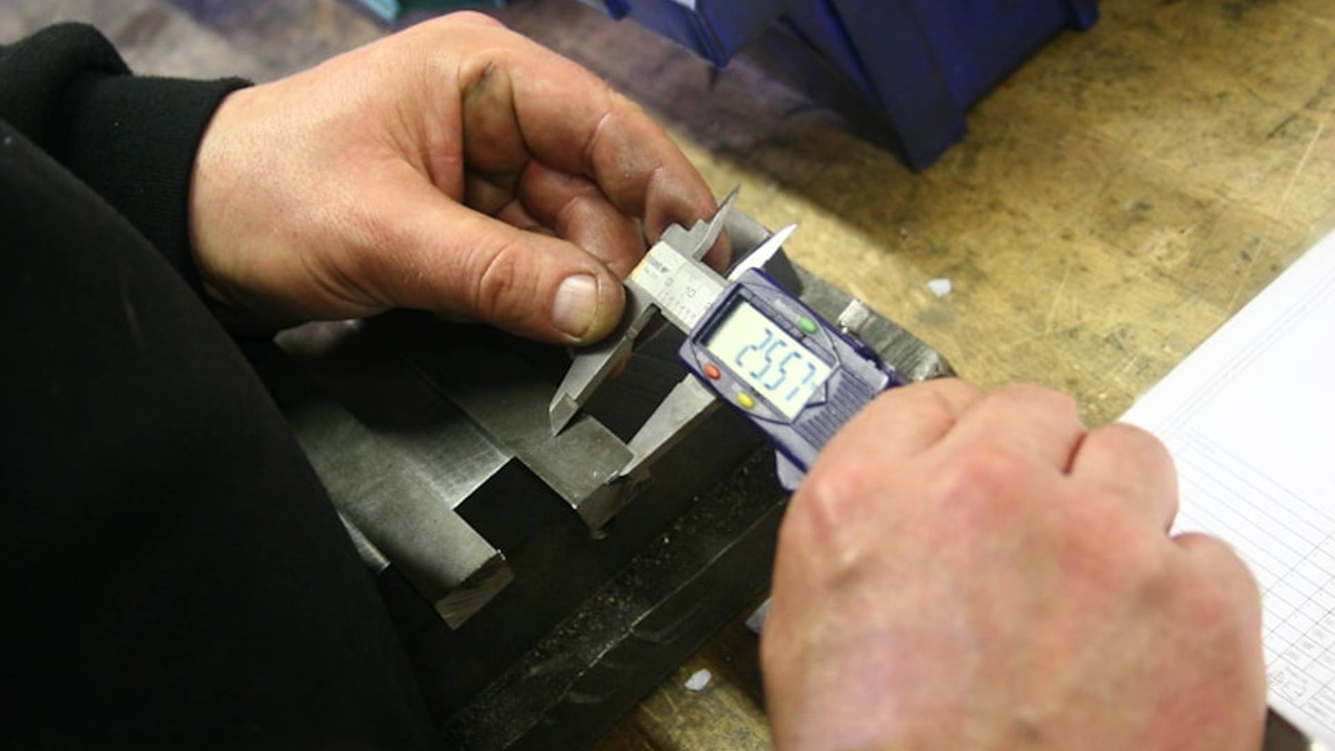 Hands using a digital caliper to measure metal part.