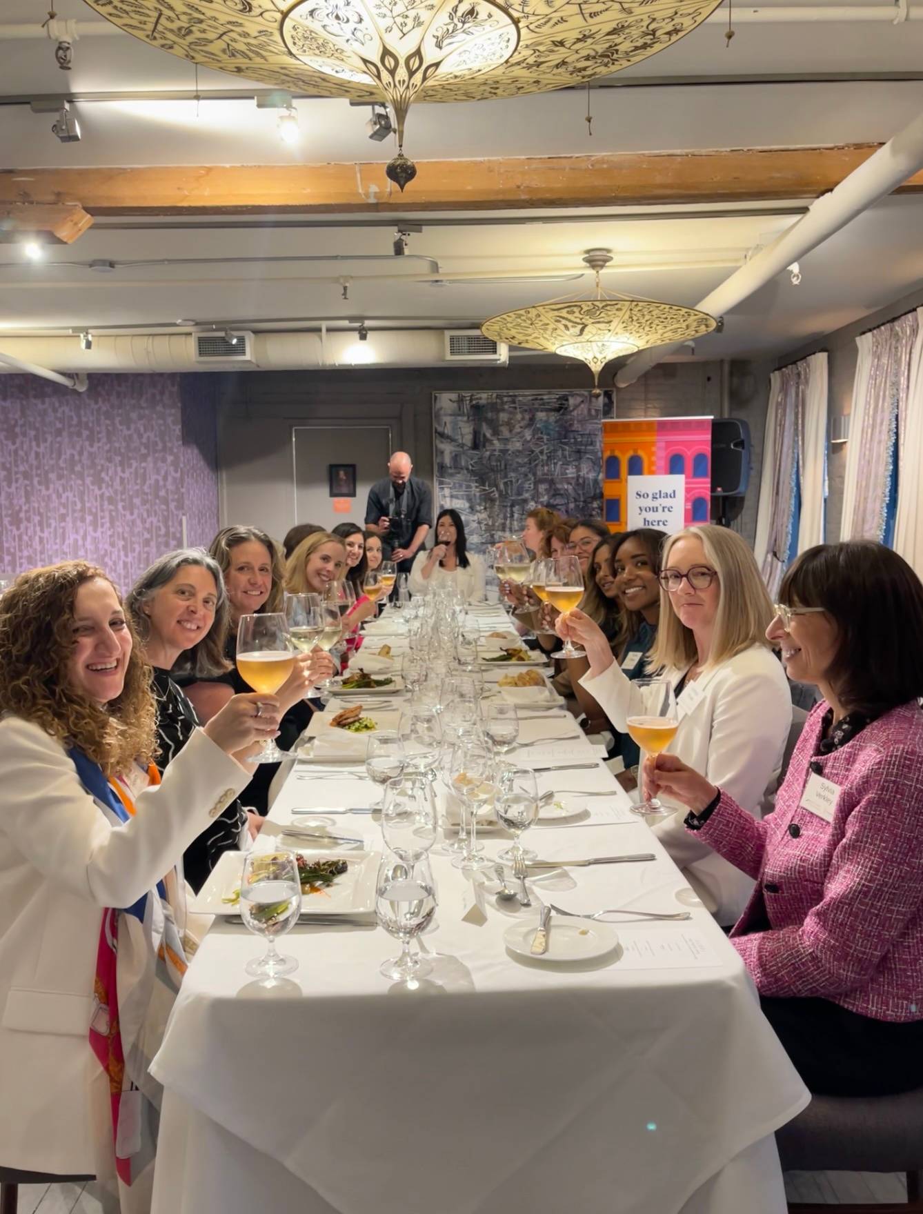 Women seated at a long table, raising wine glasses in a toast at the Verity business dining event.