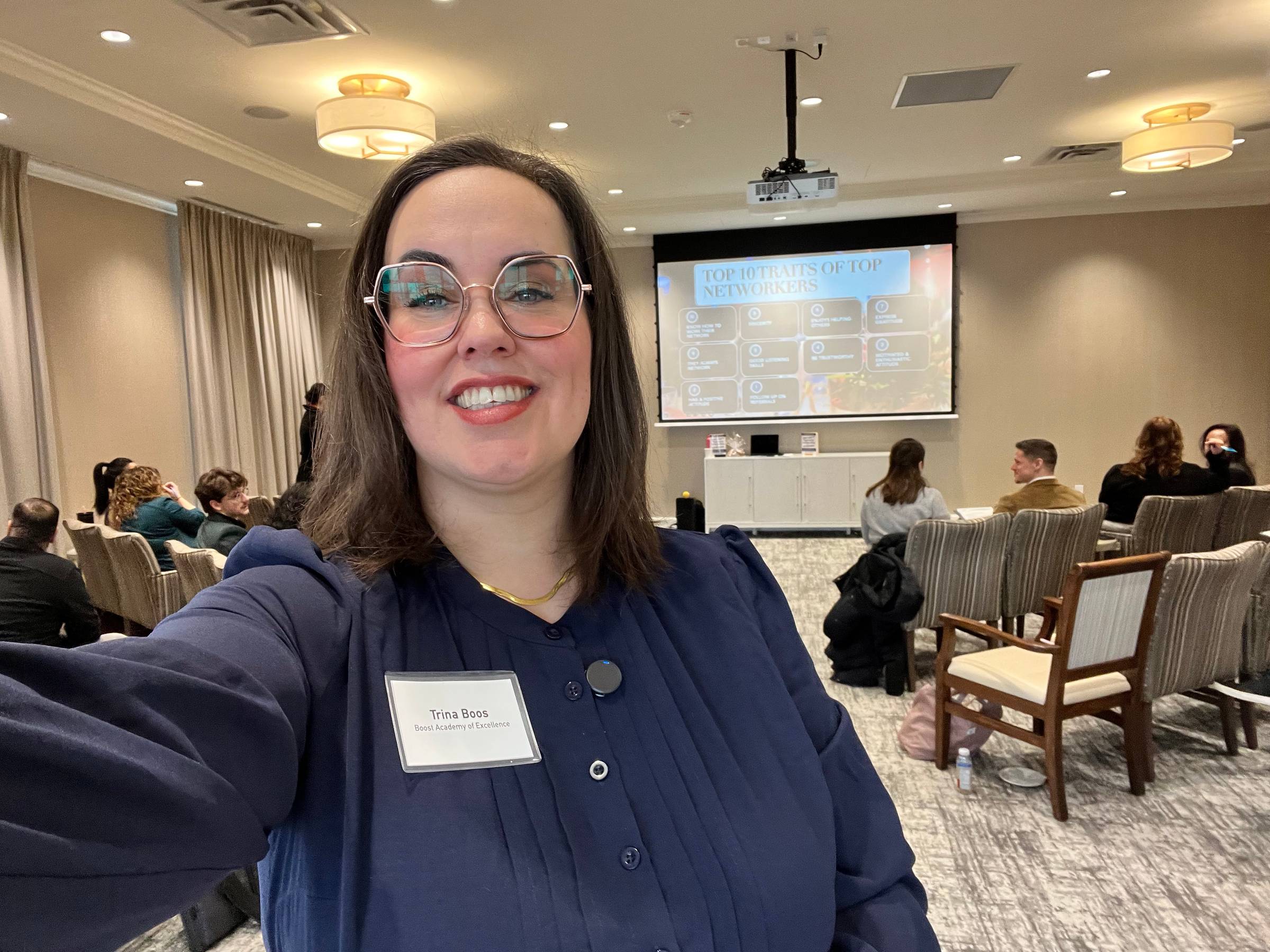 Trina Boos, founder of Boost Academy of Excellence, taking a selfie in a room before a workshop, with people on chairs sitting around her