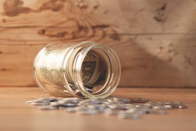 Glass jar with money and coins spilled on table