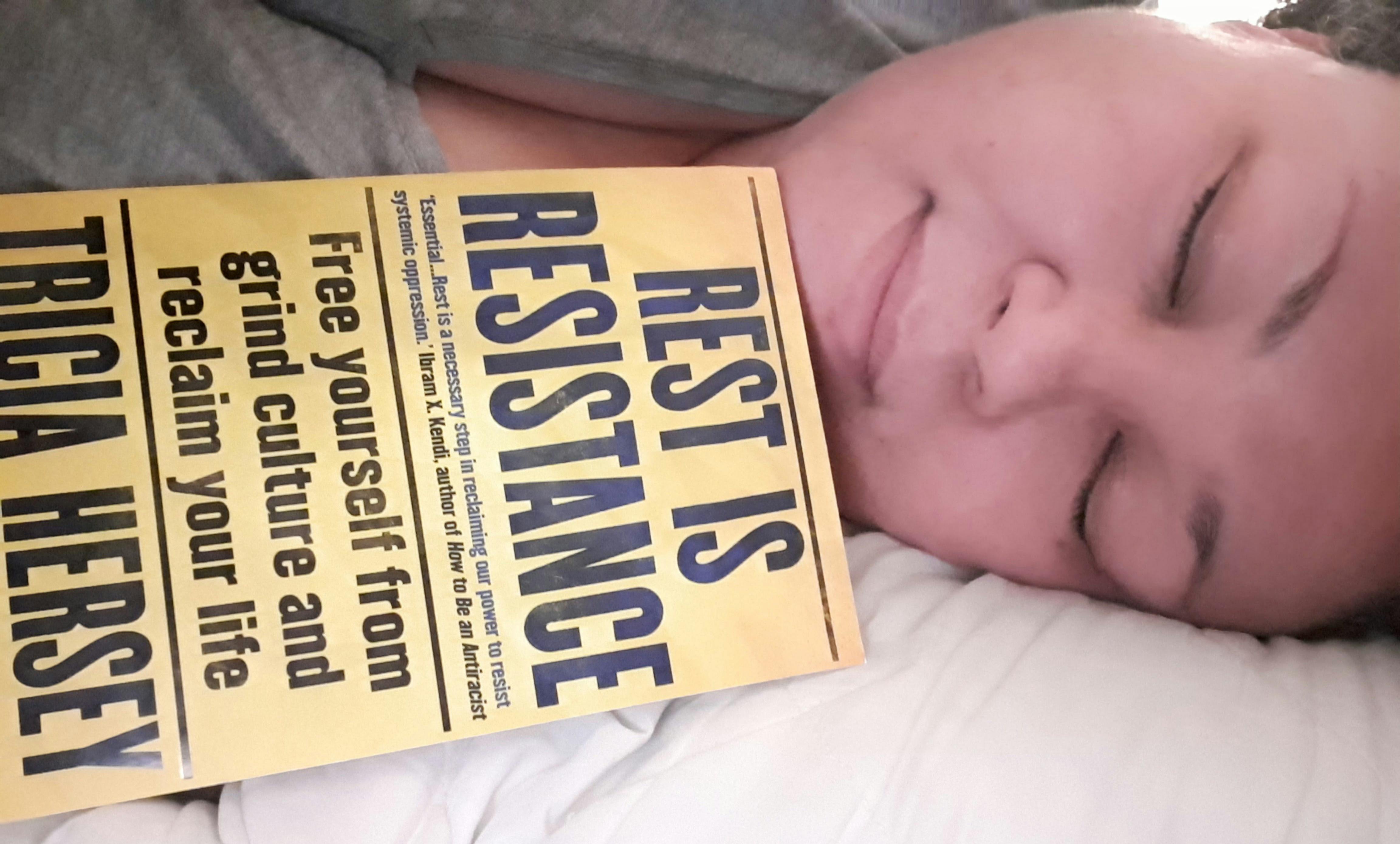 photo of a person laying down in bed with the book Rest is Resistance by Tricia Hersey