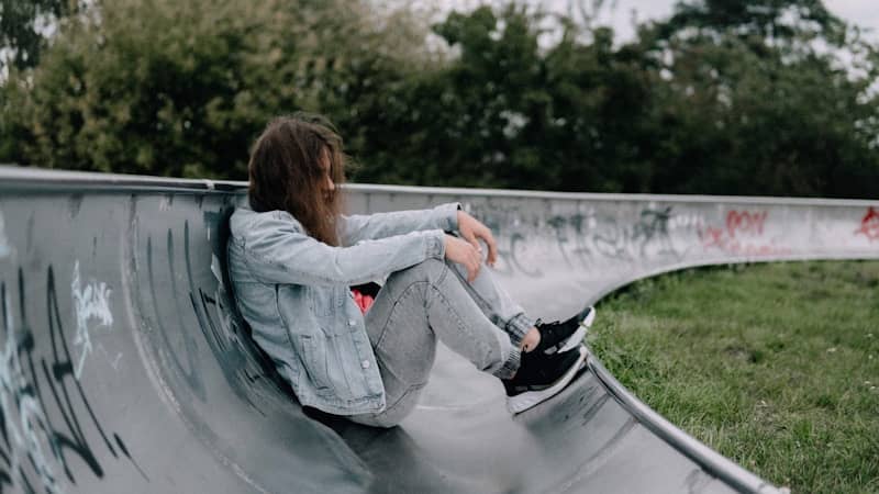 Young person sitting in a concrete skatepark bowl.