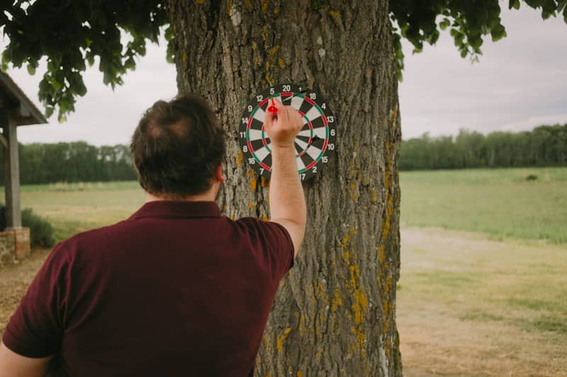 Man throwing dart at a tree-mounted dartboard.