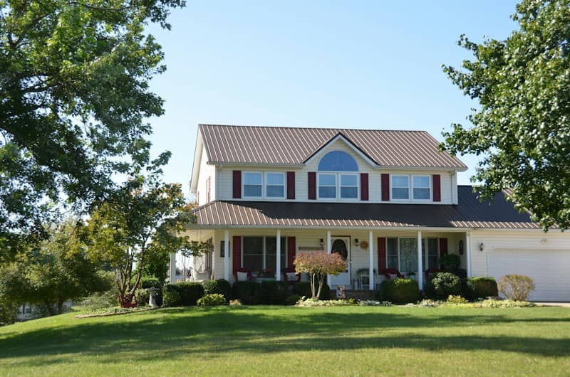 A two-story house with cream siding and a brown metal roof on a lawn