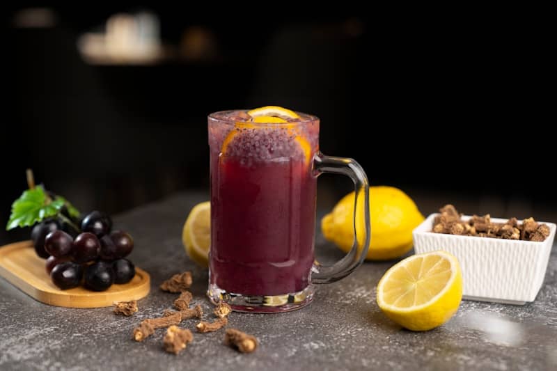A glass of red wine next to a bowl of grapes and lemons
