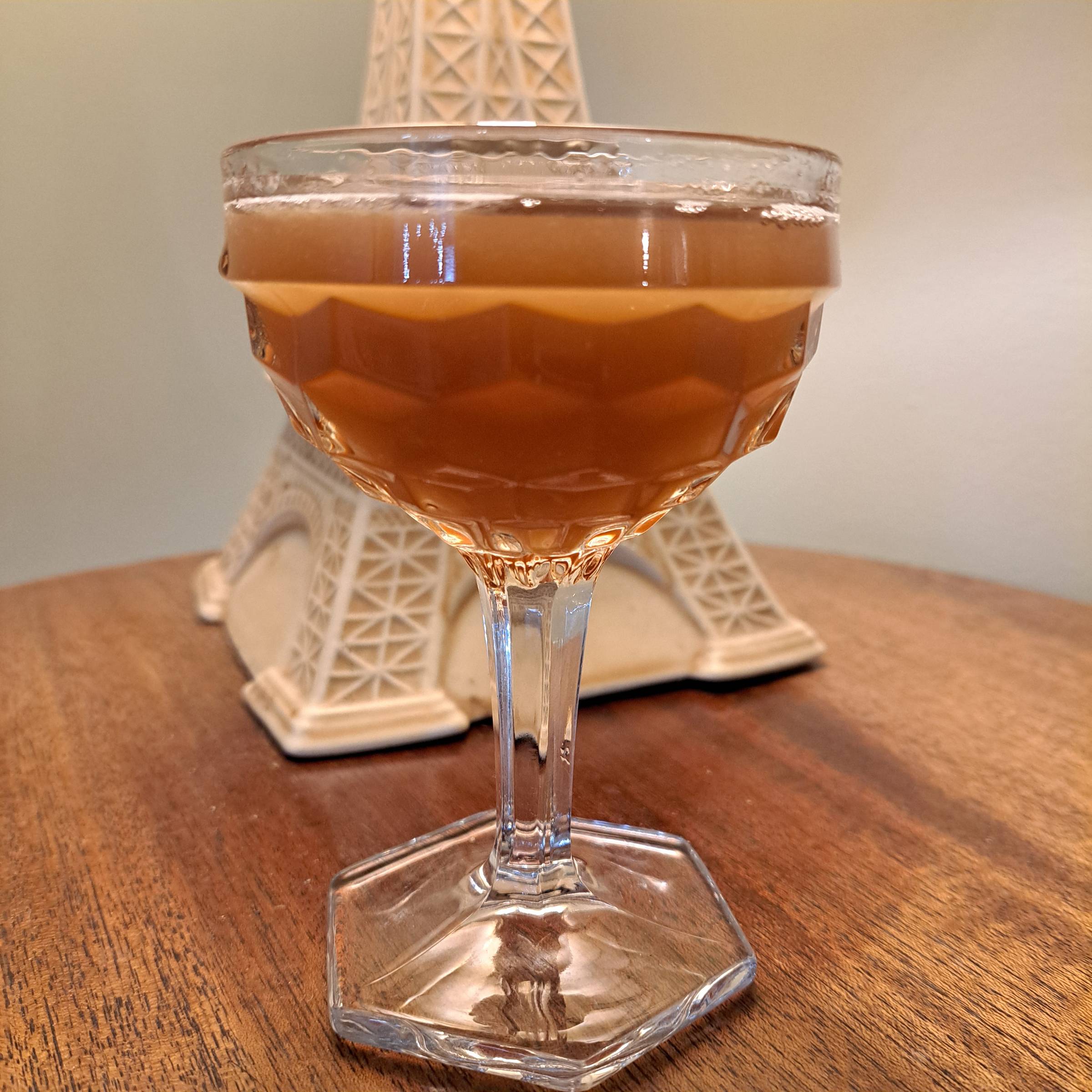 A cocktail in a fancy coupe glass in front of a kitschy Eiffel Tower lamp
