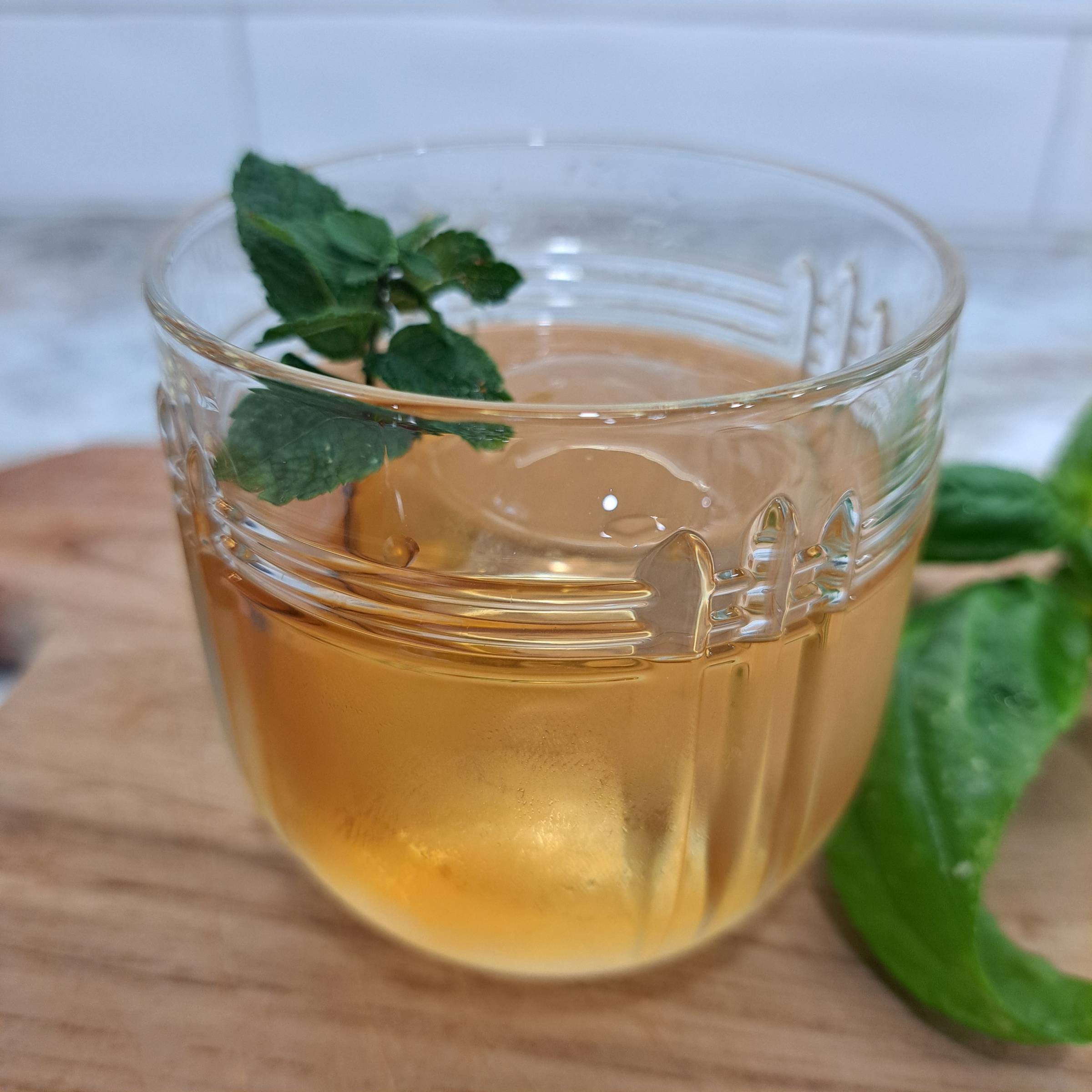 Golden herbal brandy cocktail in a cut glass with a sprig of fresh mint, served over a large ice cube on a wooden board.