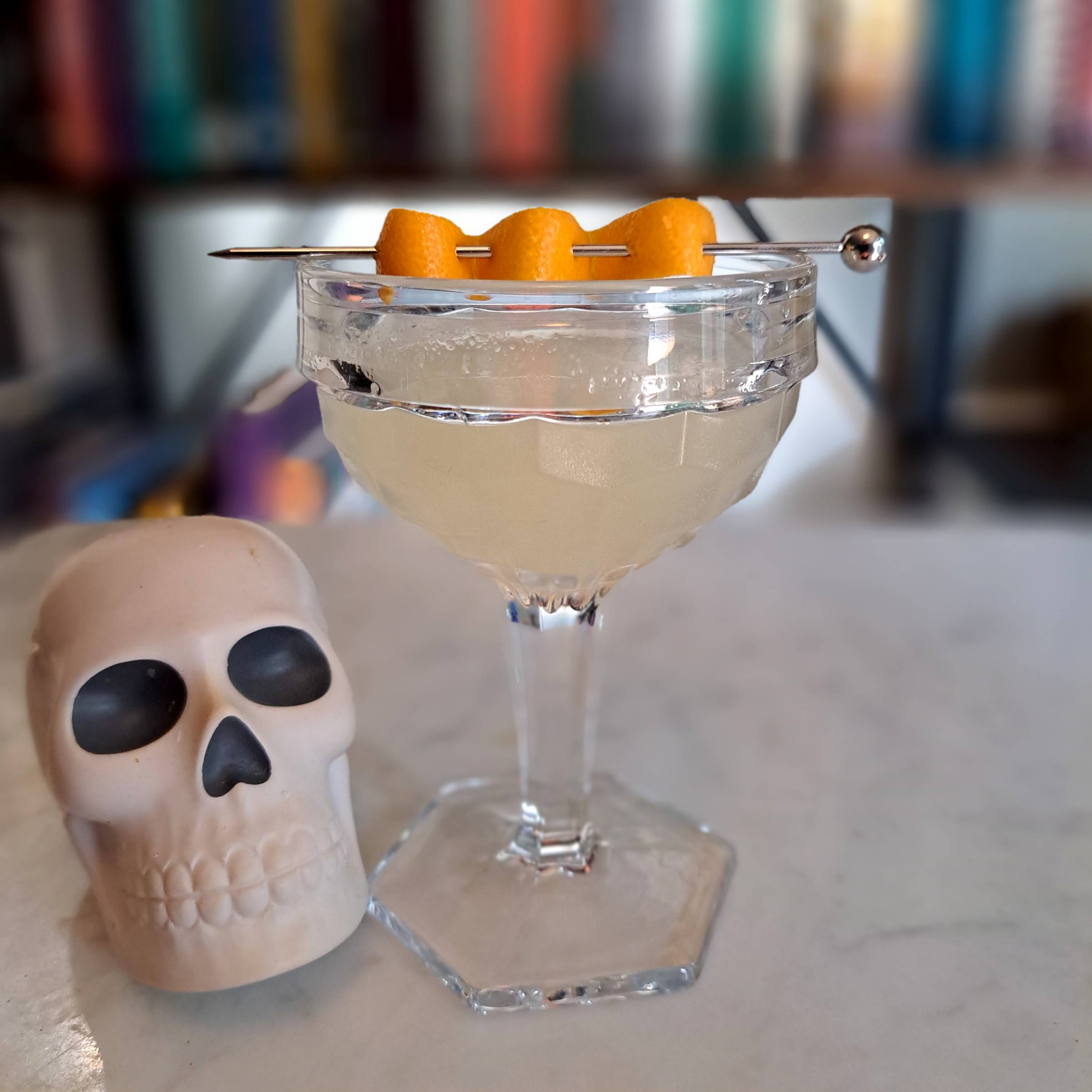 A cocktail with a fancy garnish sits on a table next to a small stylized skull
