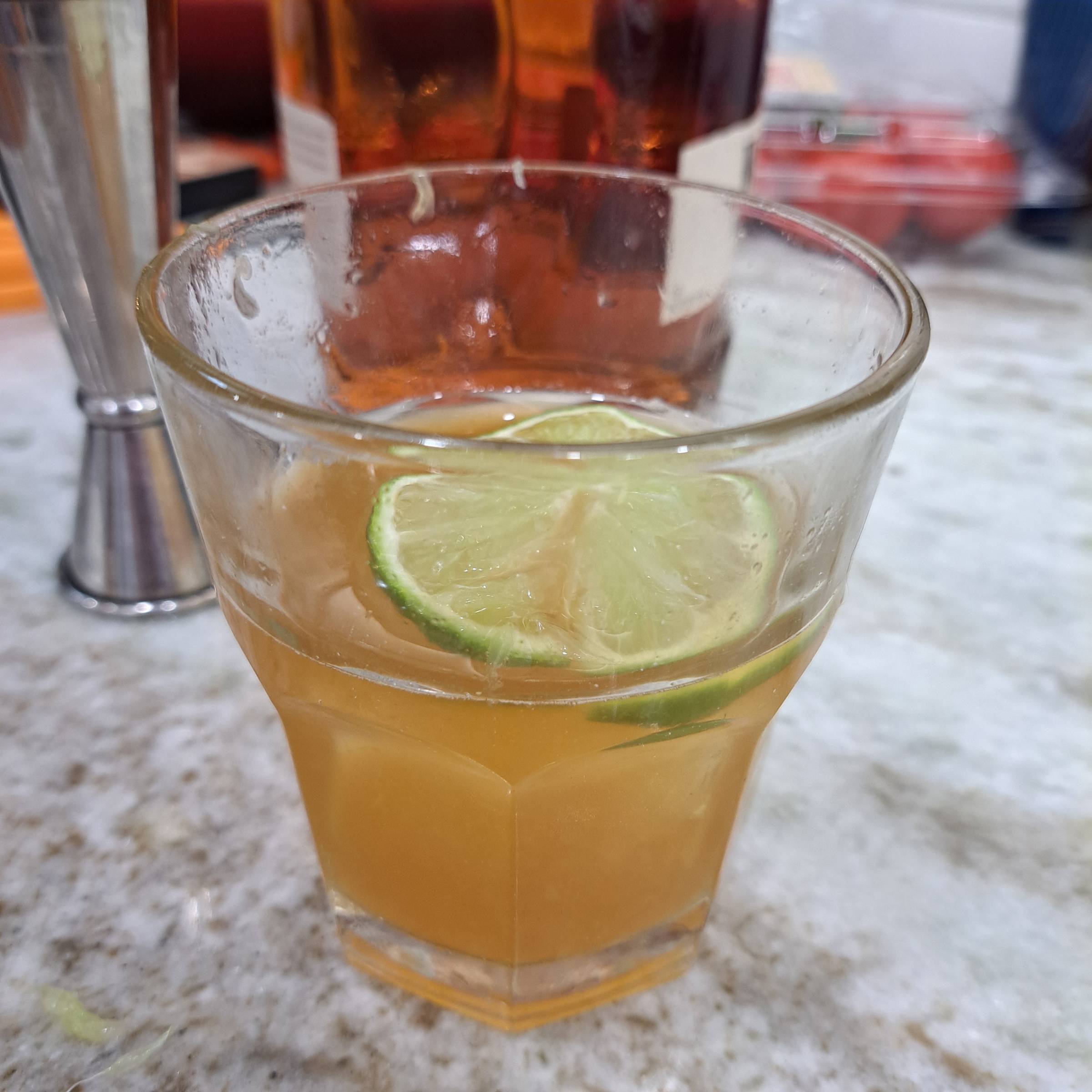 A rocks glass containing a bourbon cocktail and lime garnish