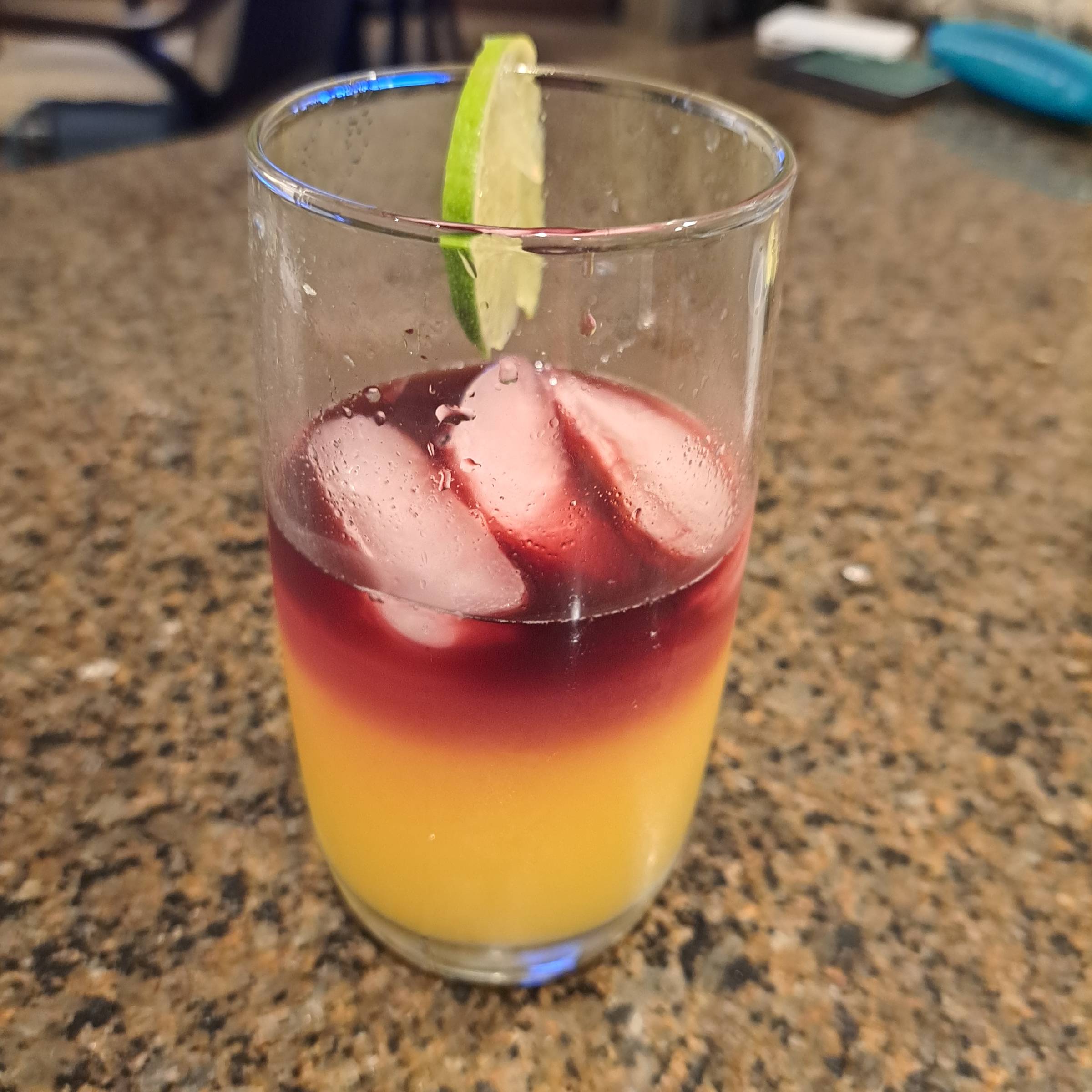 A St. John Sour cocktail with a deep red cabernet float layered over a golden tropical mixture of coconut rum, pineapple juice, orange juice, and fresh lime, served over ice in a rocks glass.