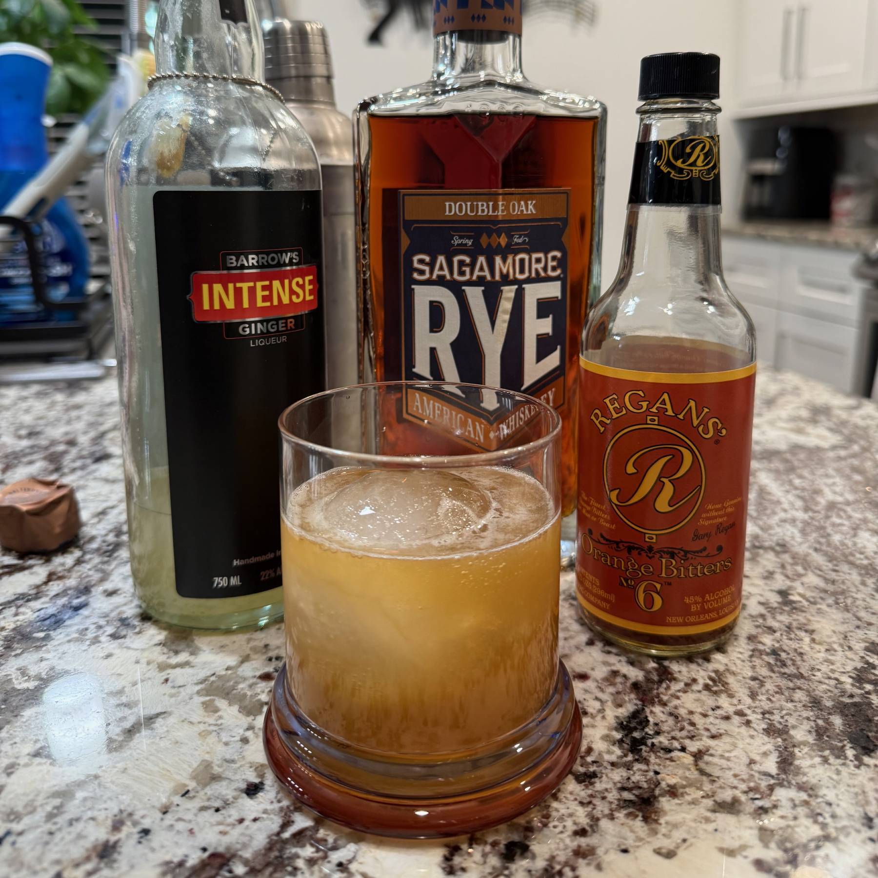 A cocktail in a rocks glass in front of three bottles of cocktail ingredients