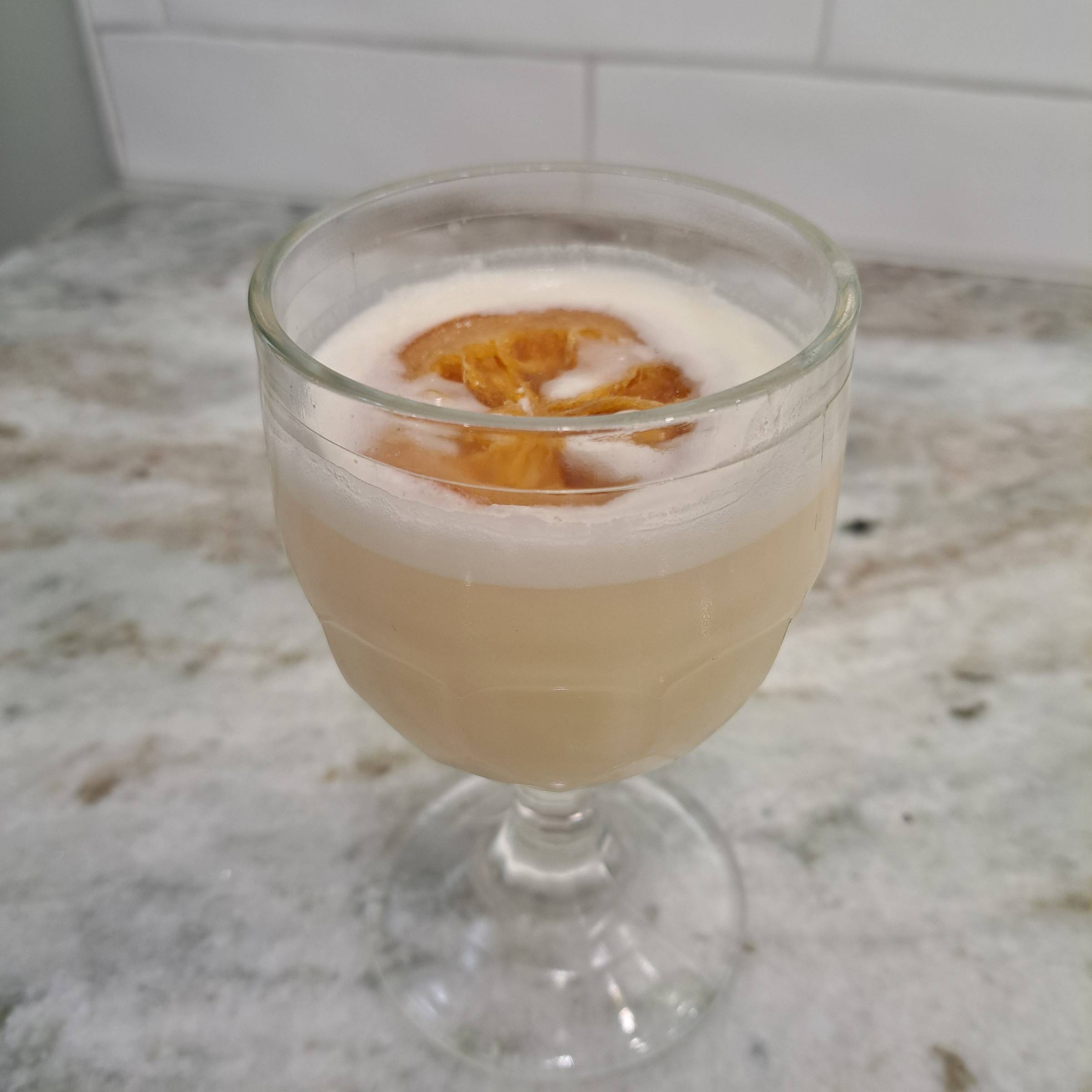 An orange creamsicle cocktail in a fancy glass with a candied orange slice floating on top