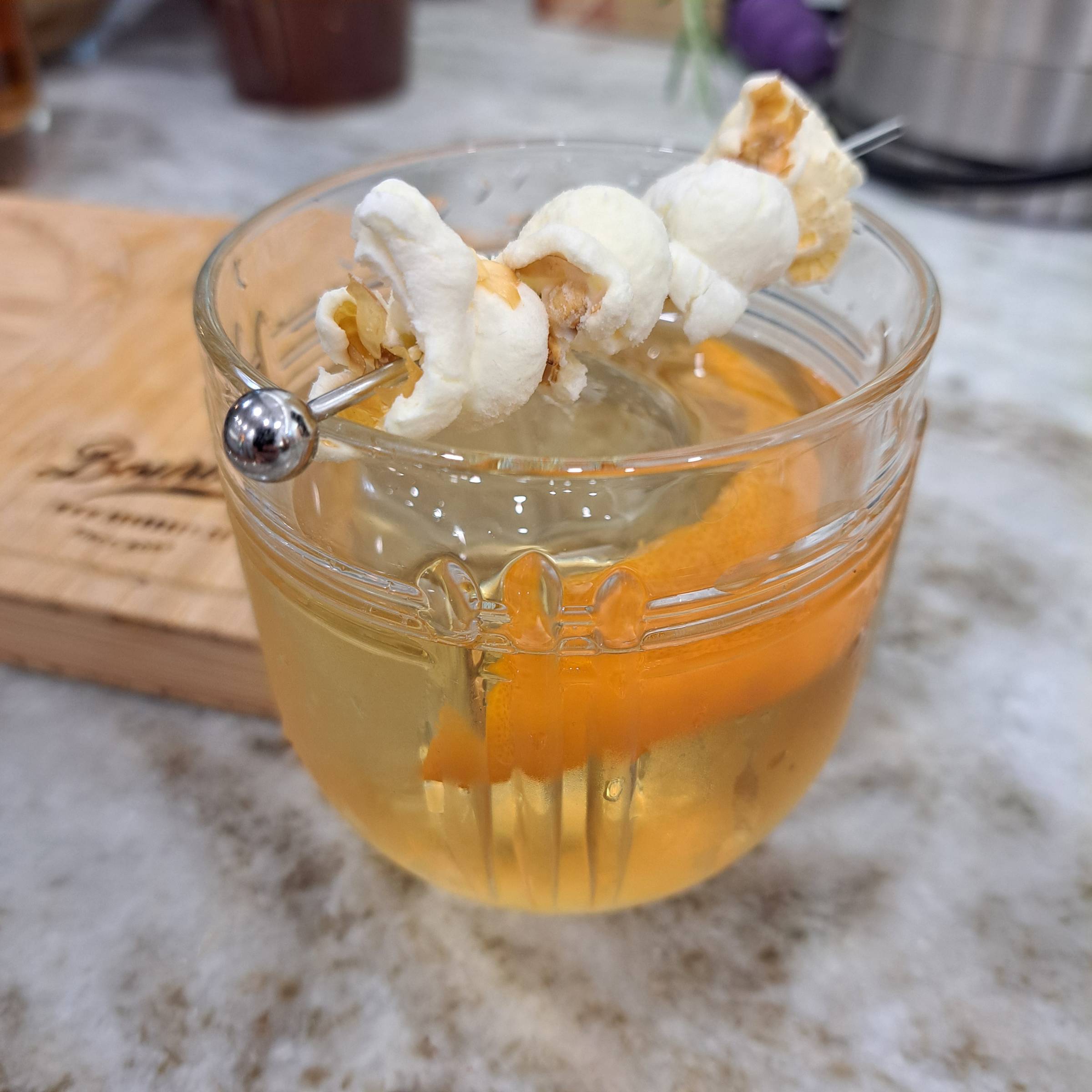 The Corny AF Old Fashioned - a bourbon cocktail garnished with a buttery popcorn skewer and an aromatic orange twist