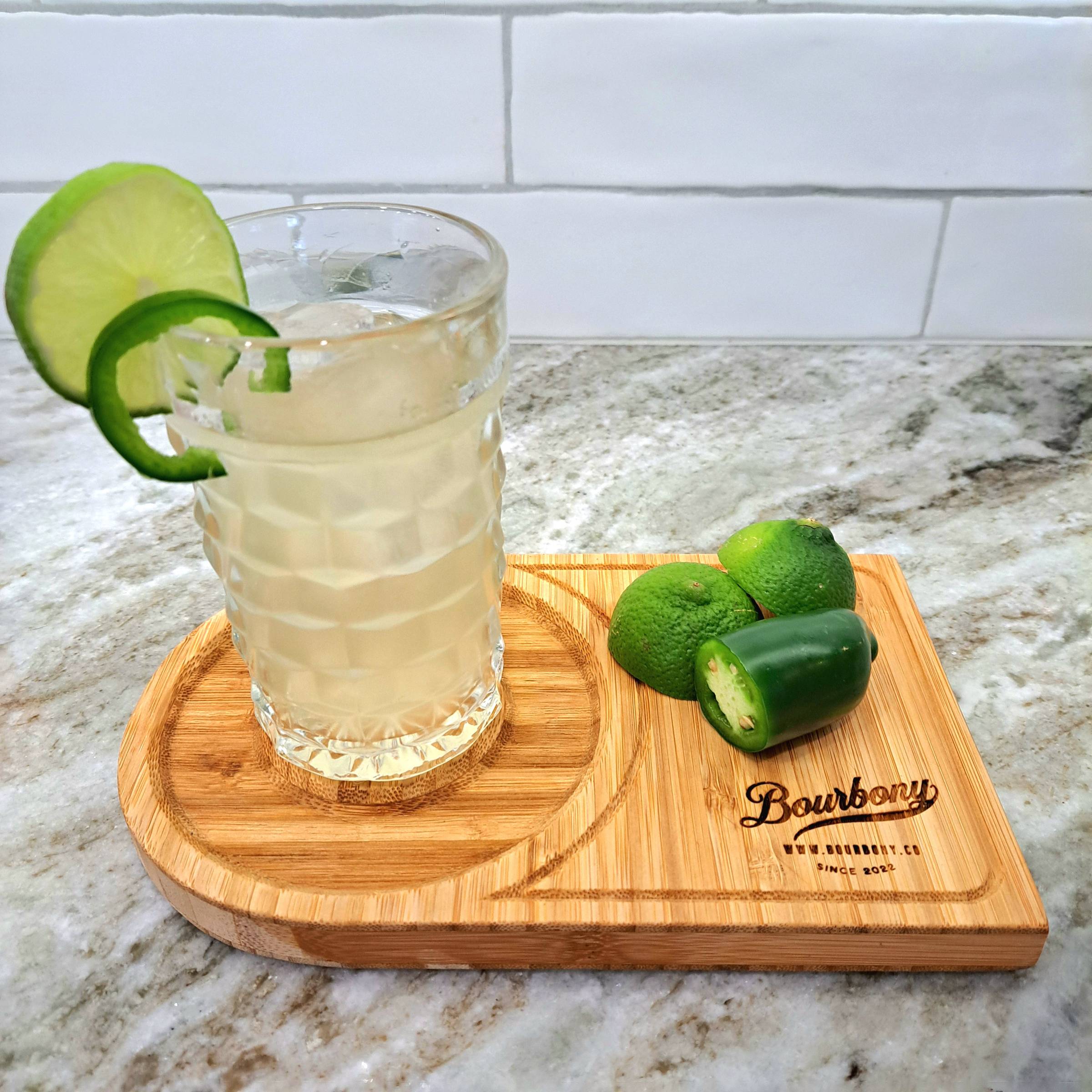 A gin and tonic on a cutting board with lime and jalapeno slices