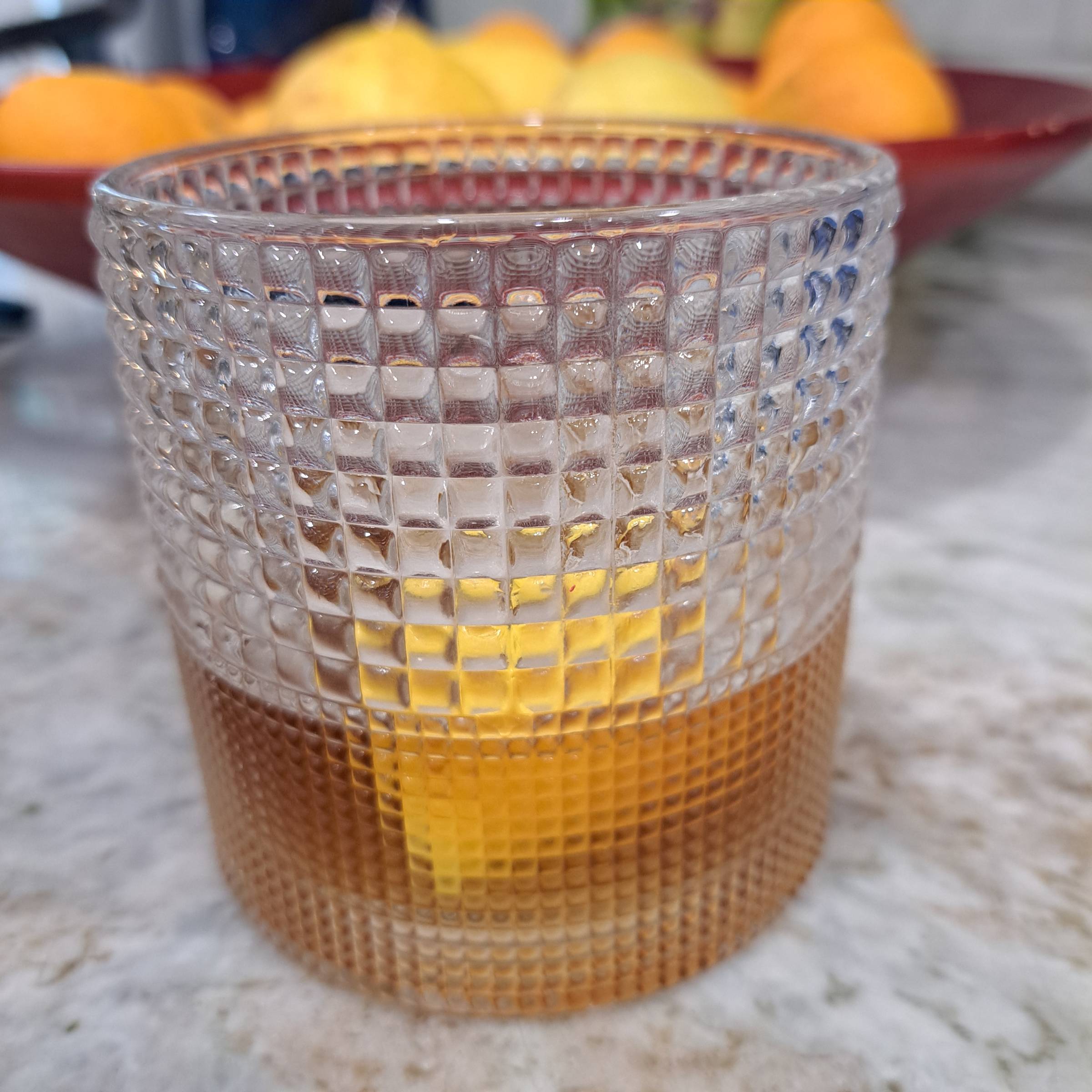 A cocktail in a fancy glass sits before a bowl of bright citrus fruit