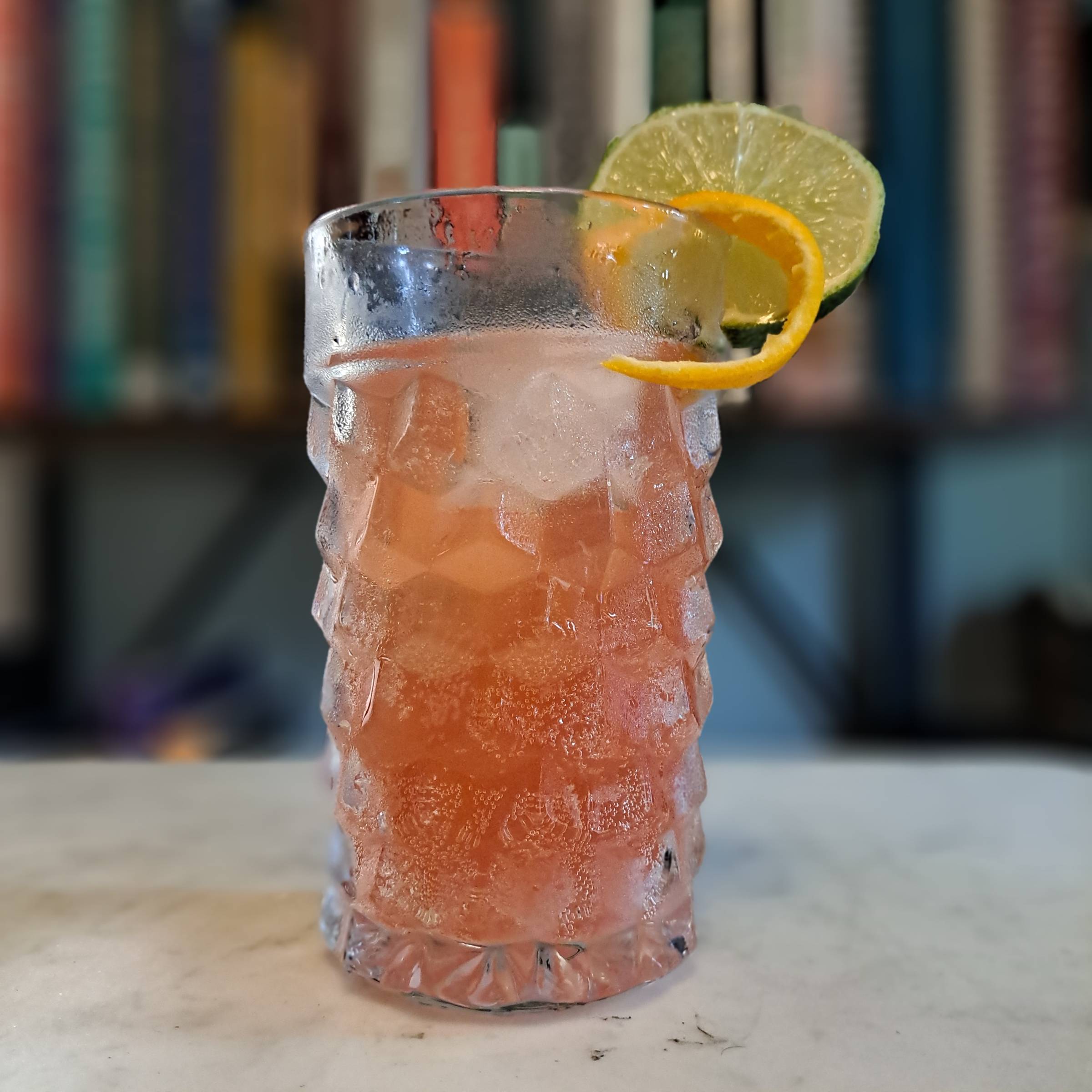 A Bourbon Campari Cocktail called The Tortie Cat served over ice with ginger beer, an expressed orange peel, and a fresh lime wheel garnish.