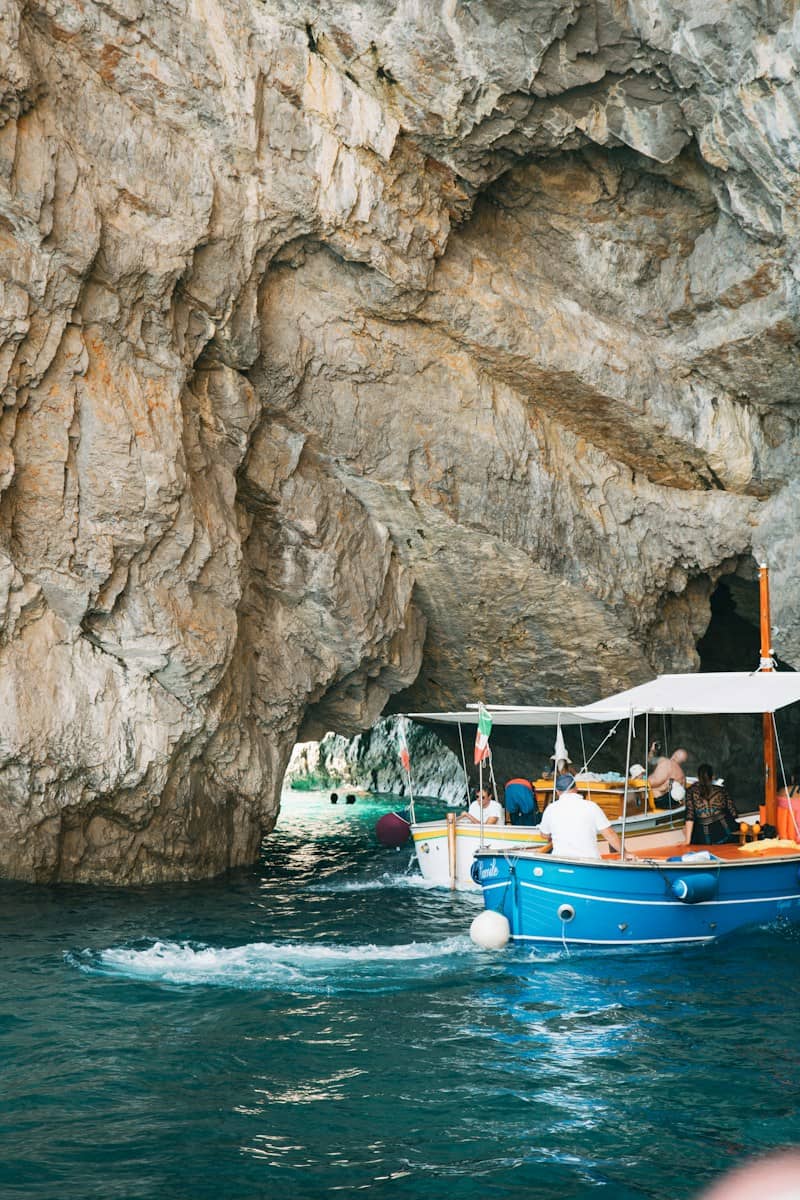 Boats navigate through a large rock archway in turquoise water.