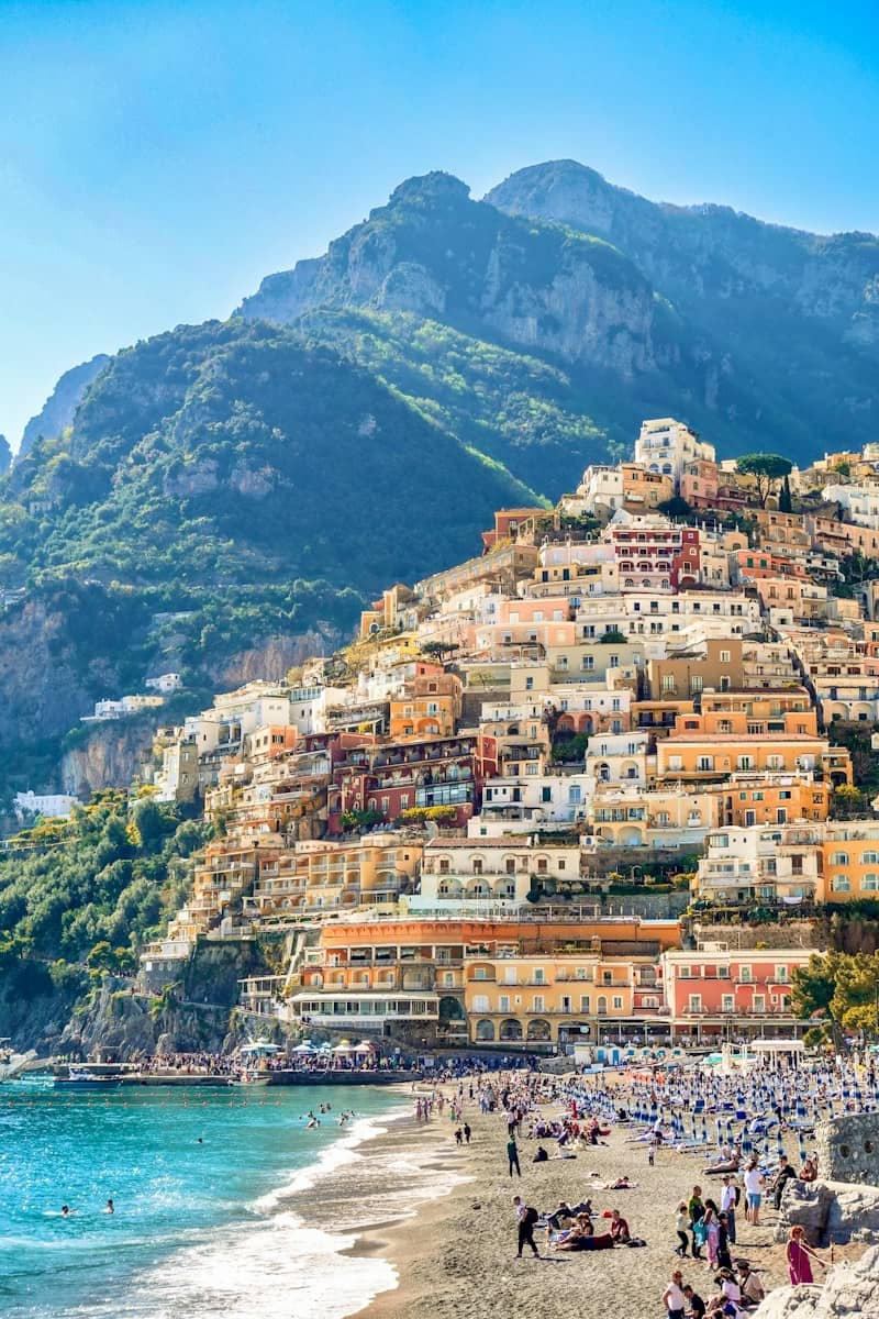 Colorful buildings cascade down a mountain to a crowded beach.