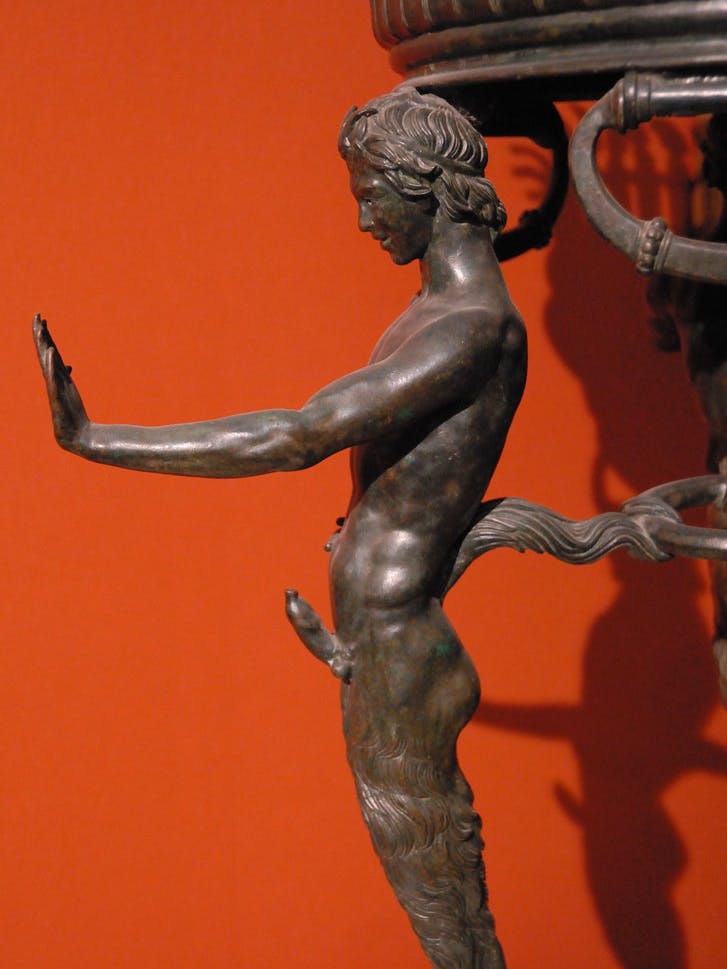 close up of a bronze tripod decorated with a muscular young man sporting a erection