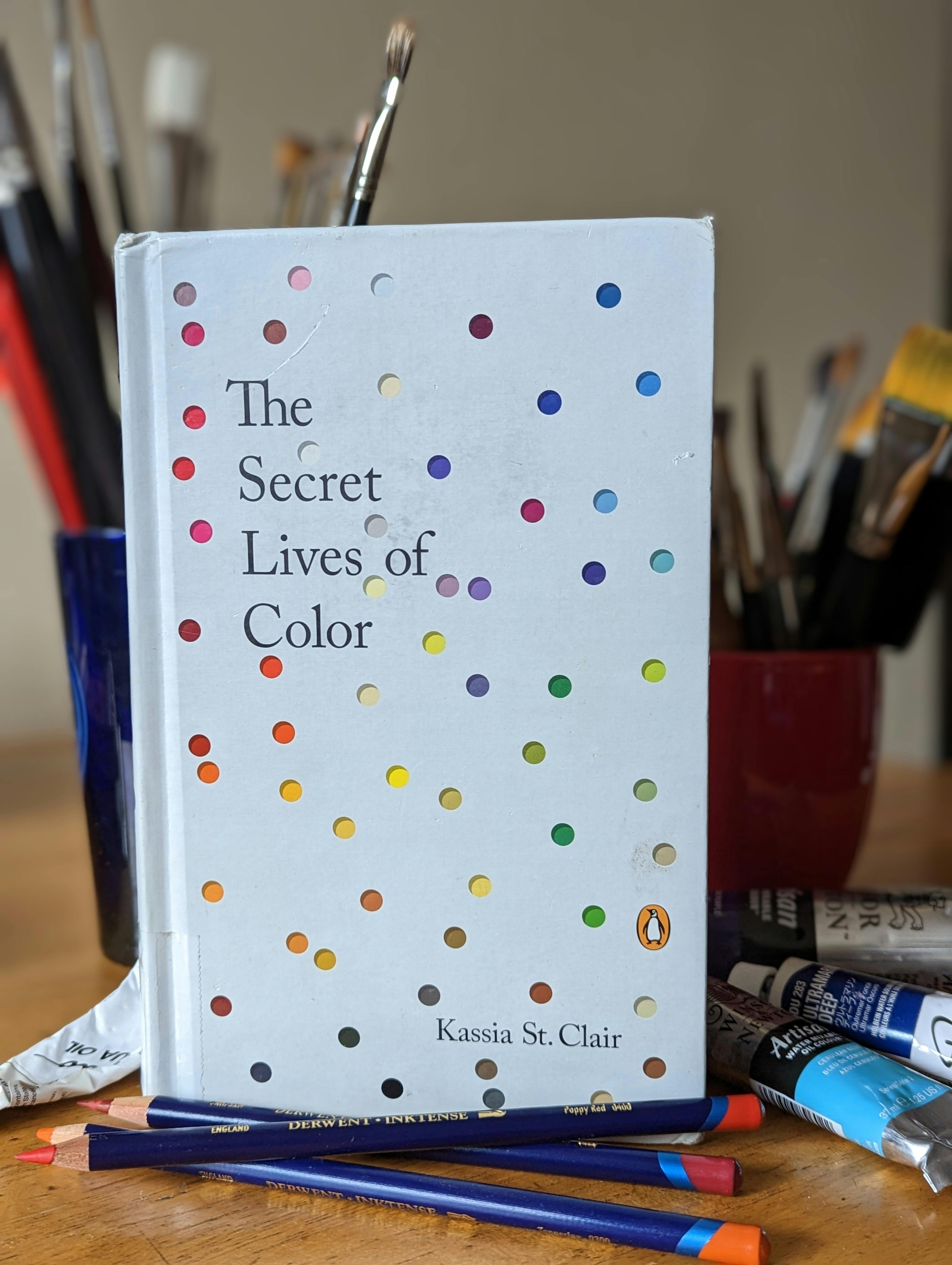 cover of the book The Secret Lives of Color by Kassia St. Clair; a field of pure white speckled with tiny dots of color 