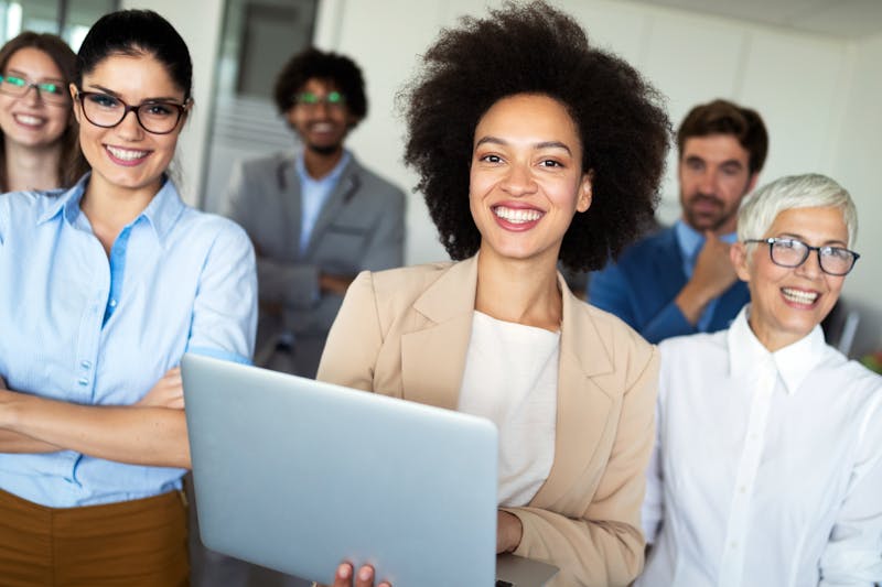 Woman smiling holding a computer in front of a diverse group of people smiling 