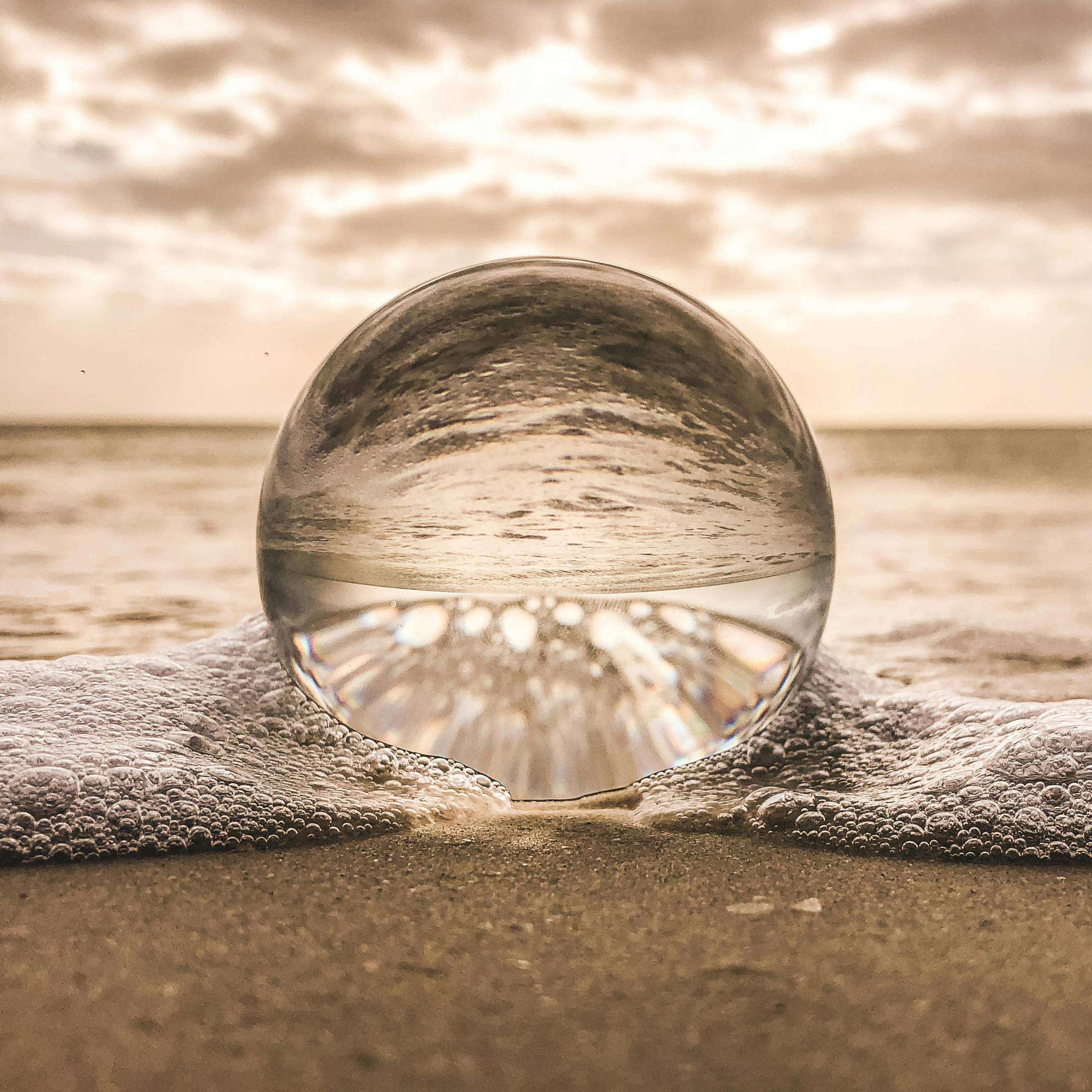 glass ball on sandy beach reflecting the body of water