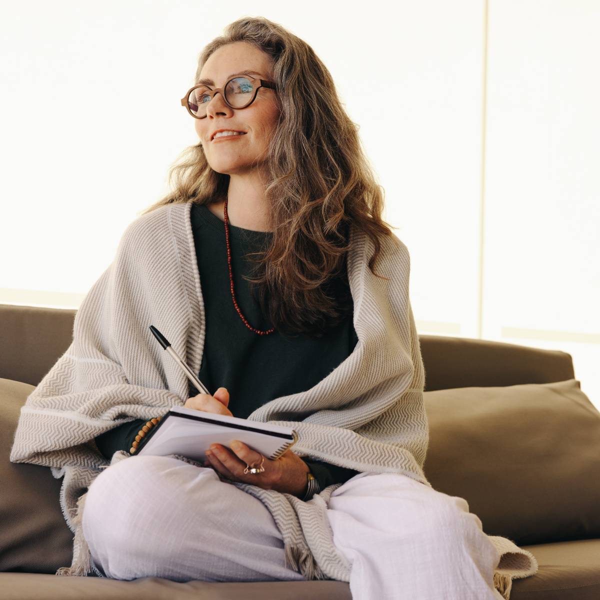 Woman with brown wavy hair and glasses in shawl holding journal