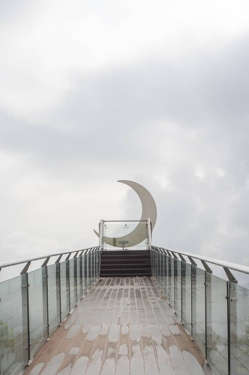 A crescent moon sculpture on a walkway under cloudy skies