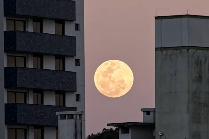 Full moon visible between two buildings at dusk.