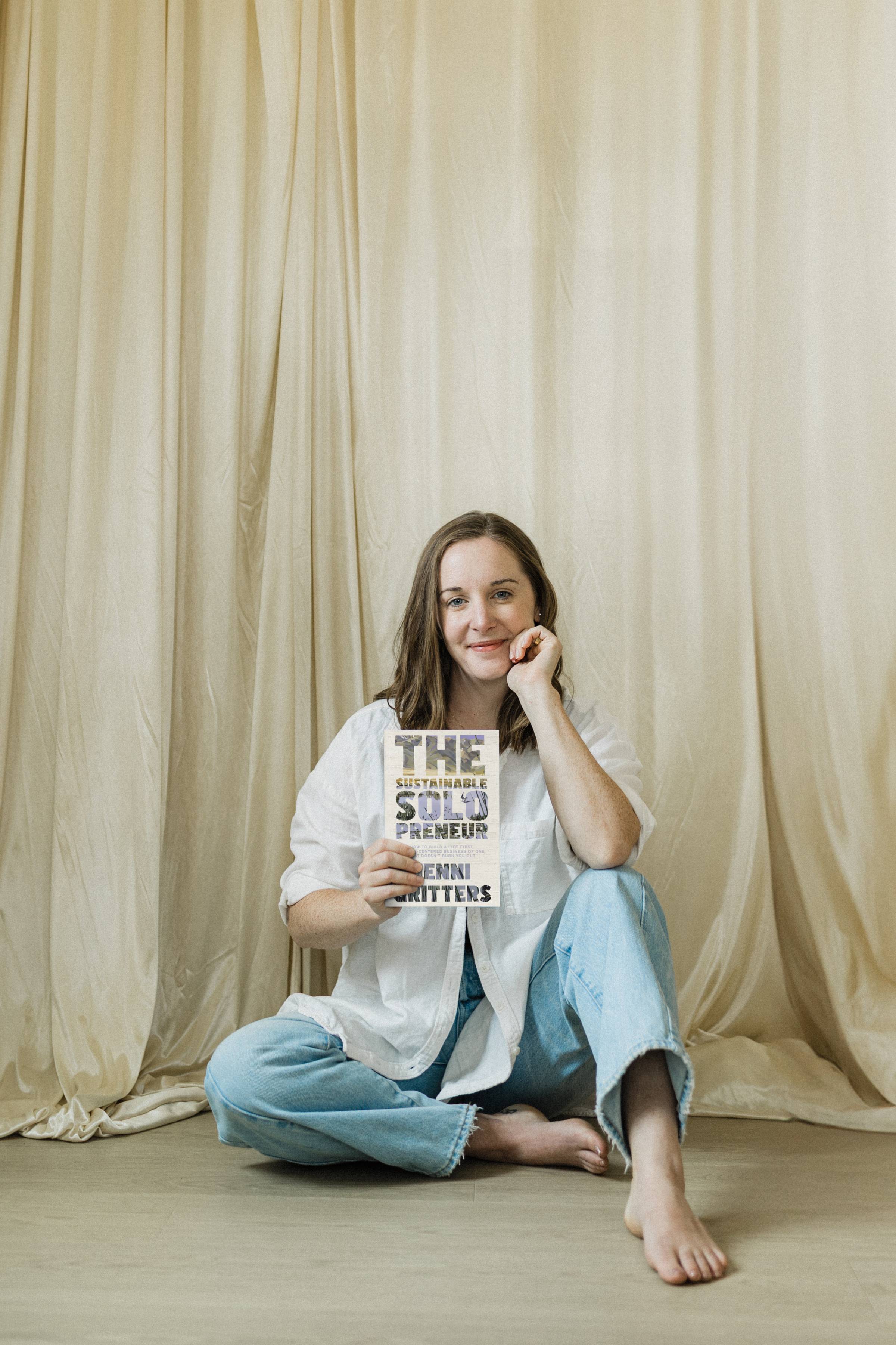 Jenni Gritters is sitting on the floor holding up a copy of her book