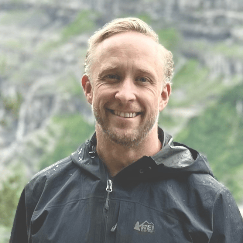 Matt hill is standing outside wearing an REI coat. He is smiling at the camera.