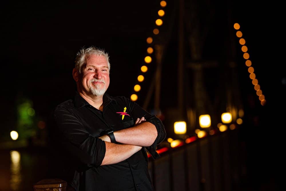 Mike, a white man, stands with his arms crossed and is smiling at the camera. 