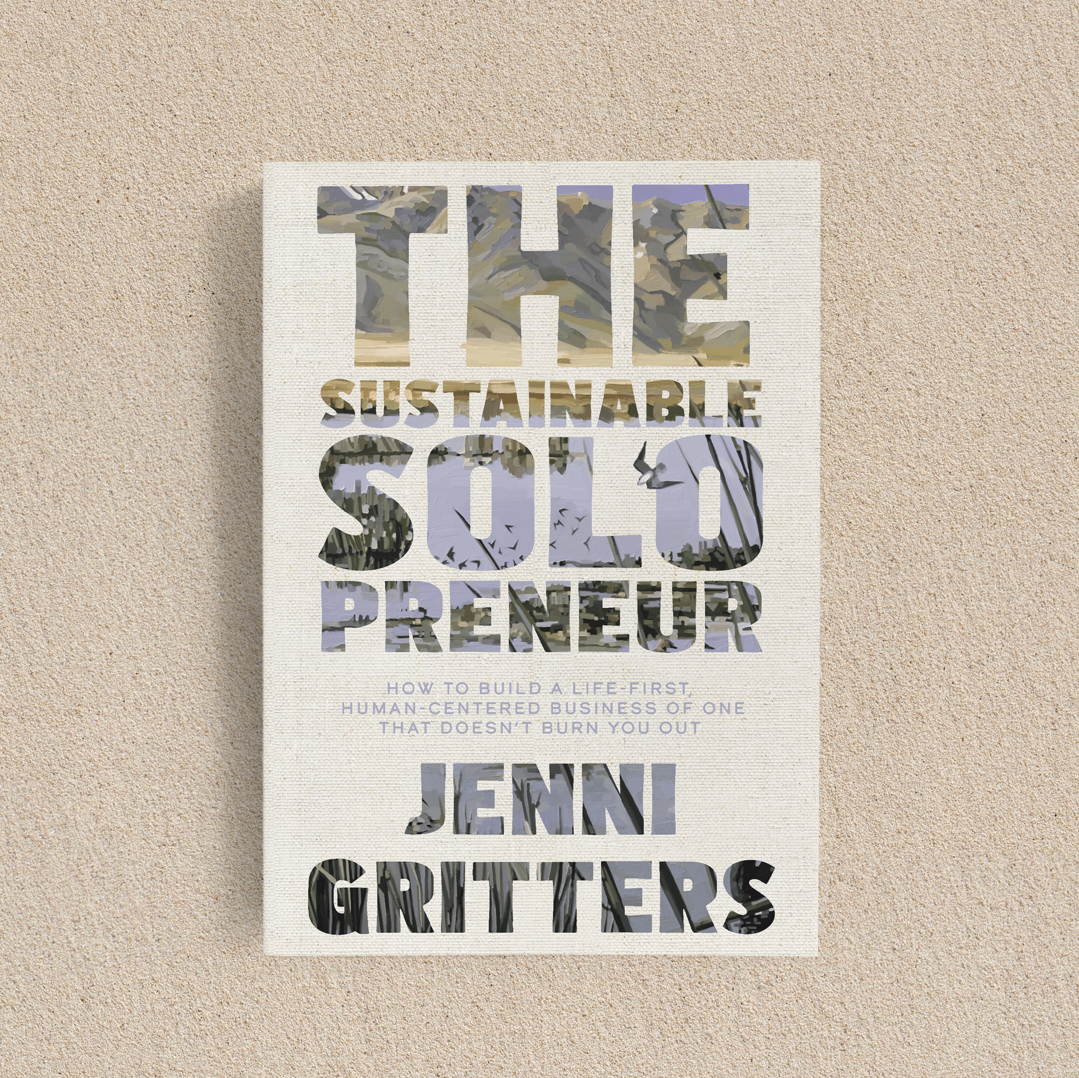 The book is sitting on the sand. The cover is a cream color, and the book title has cut-out letters that show a painting of a thriving landscape.
