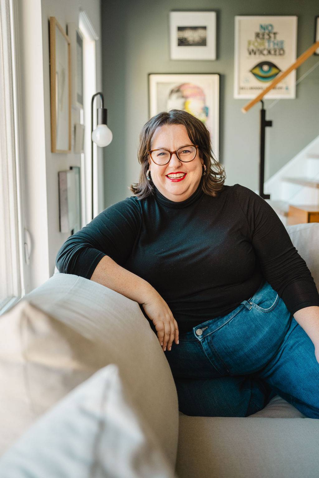 Amanda is a white woman with shoulder-length brown hair sitting on a couch with artwork in the background.