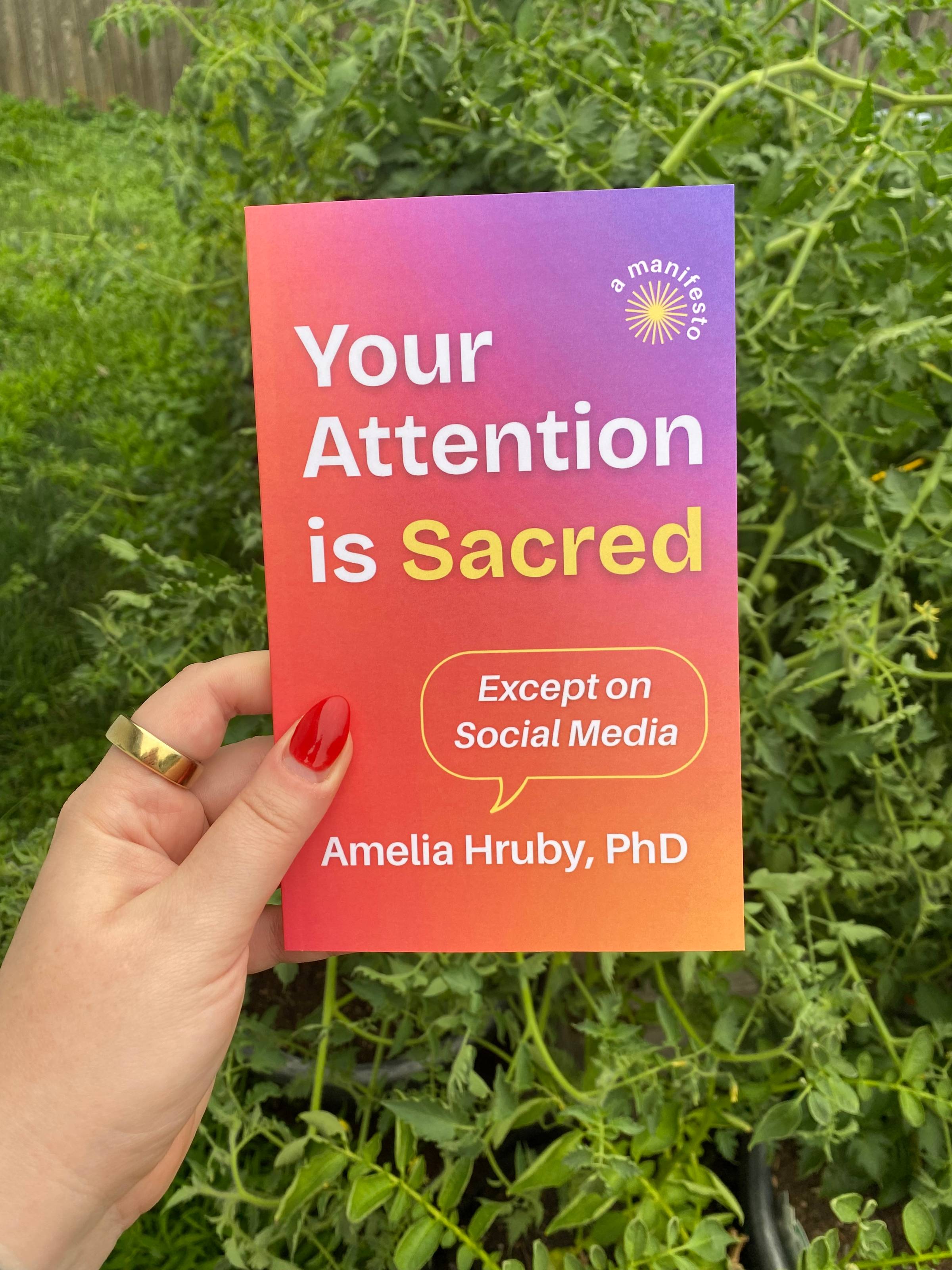 A picture of a hand with a bright red nail holding a copy of Amelia's book against a background of plants.
