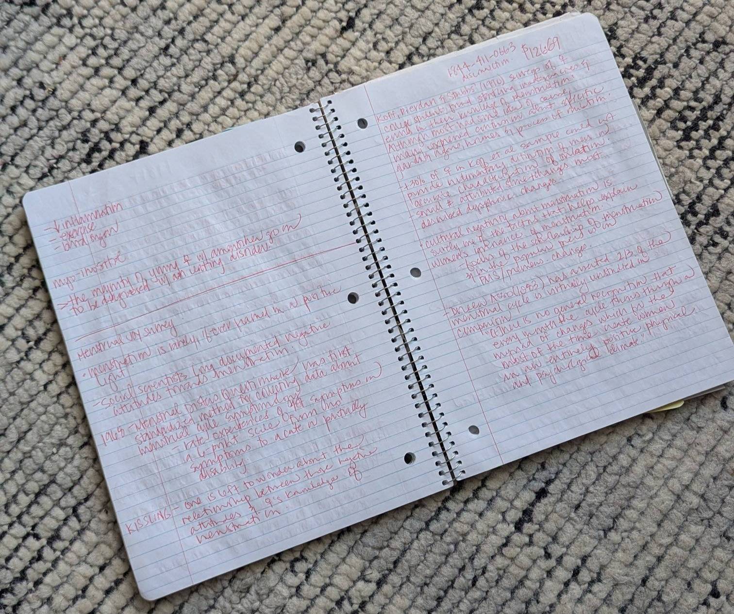 Amanda's spiral-bound notebook is open, showcasing draft writing in bright red ink.