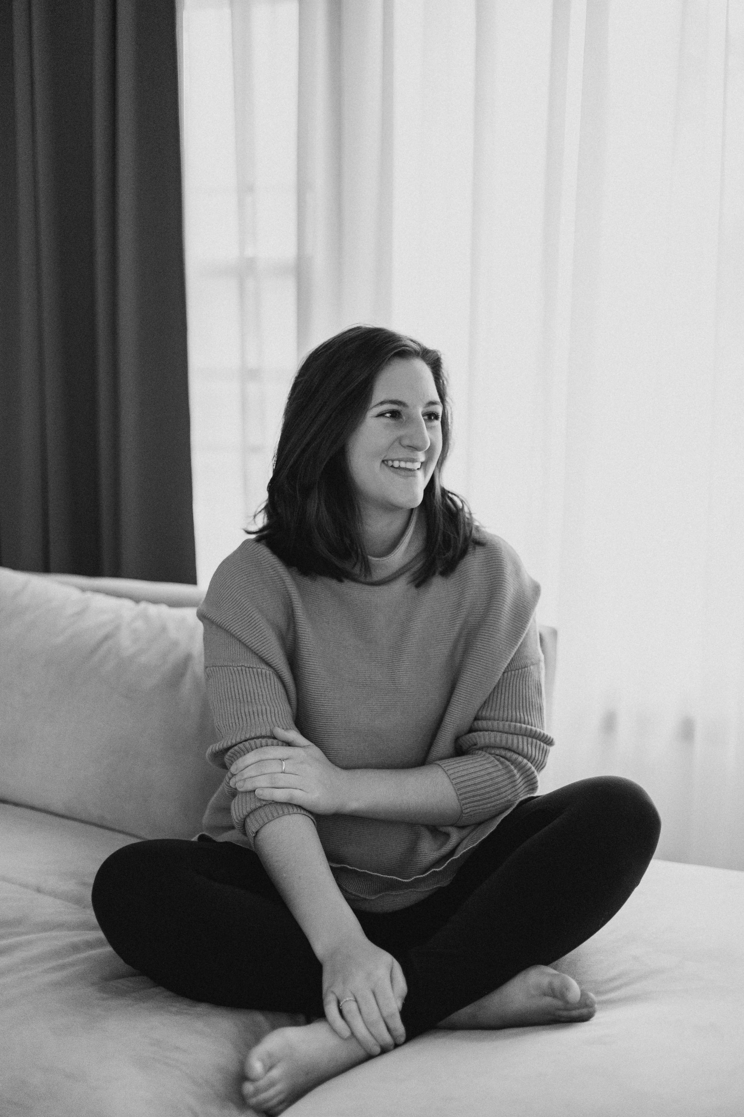 A black and white photo of Kasia Manolas, sitting on a sofa