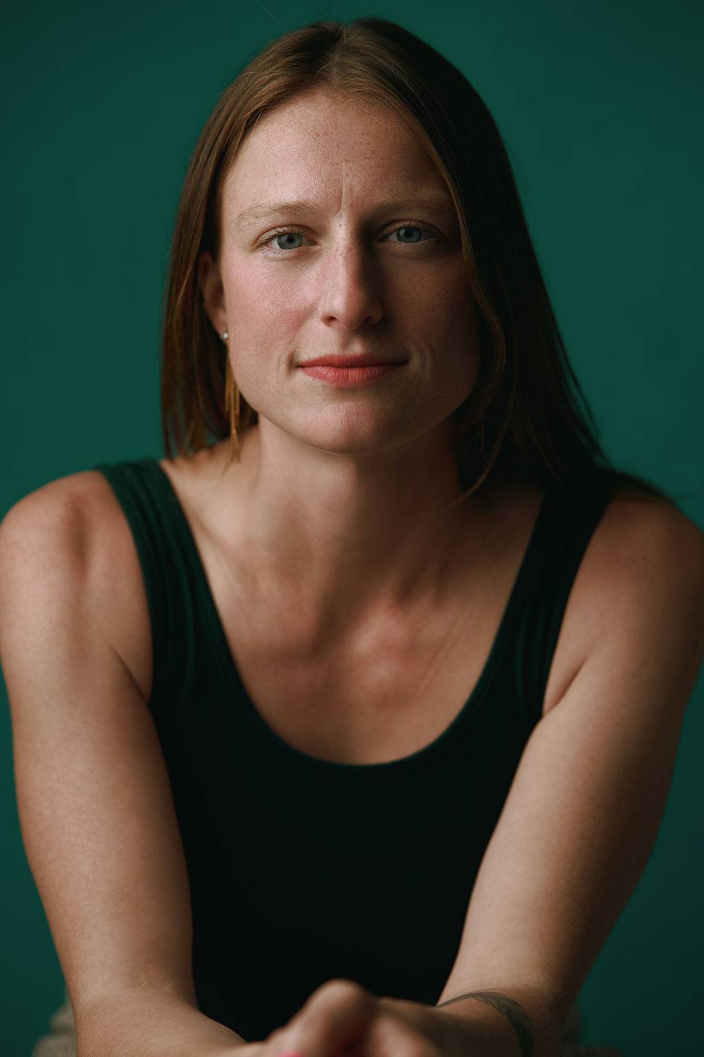 Angie Marie has sandy hair and blue eyes. She is pictured against a dark green background with an intent but open expression.