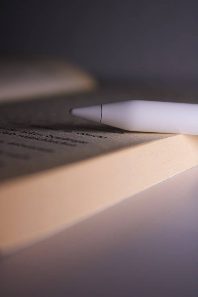 A white stylus rests on an open book.